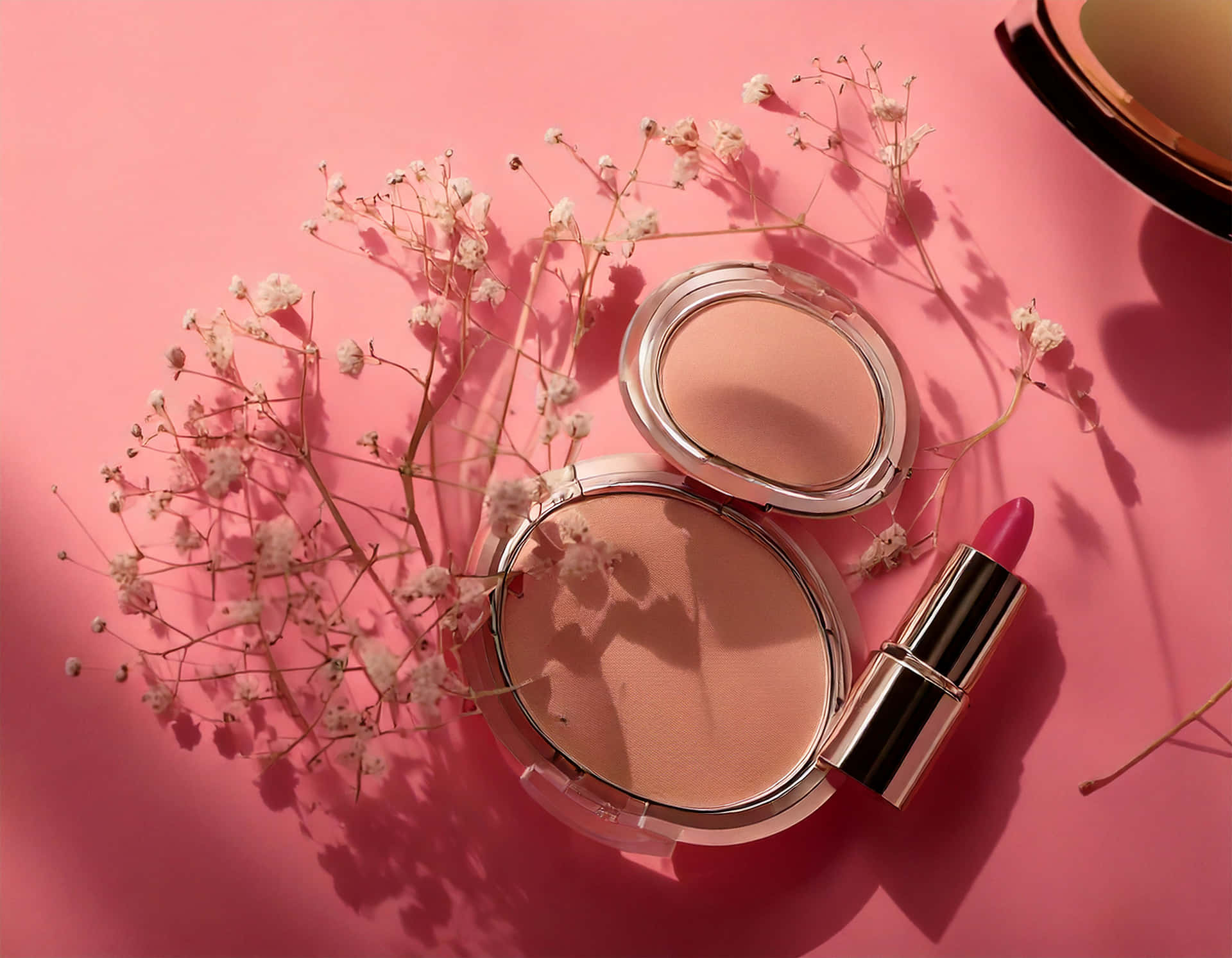 Minimalist flat-lay of a compact powder and lipstick 壁紙 — 柔軟的粉紅色背景上，打開的化妝粉盒和一支口紅被精緻的滿天星花朵環繞。