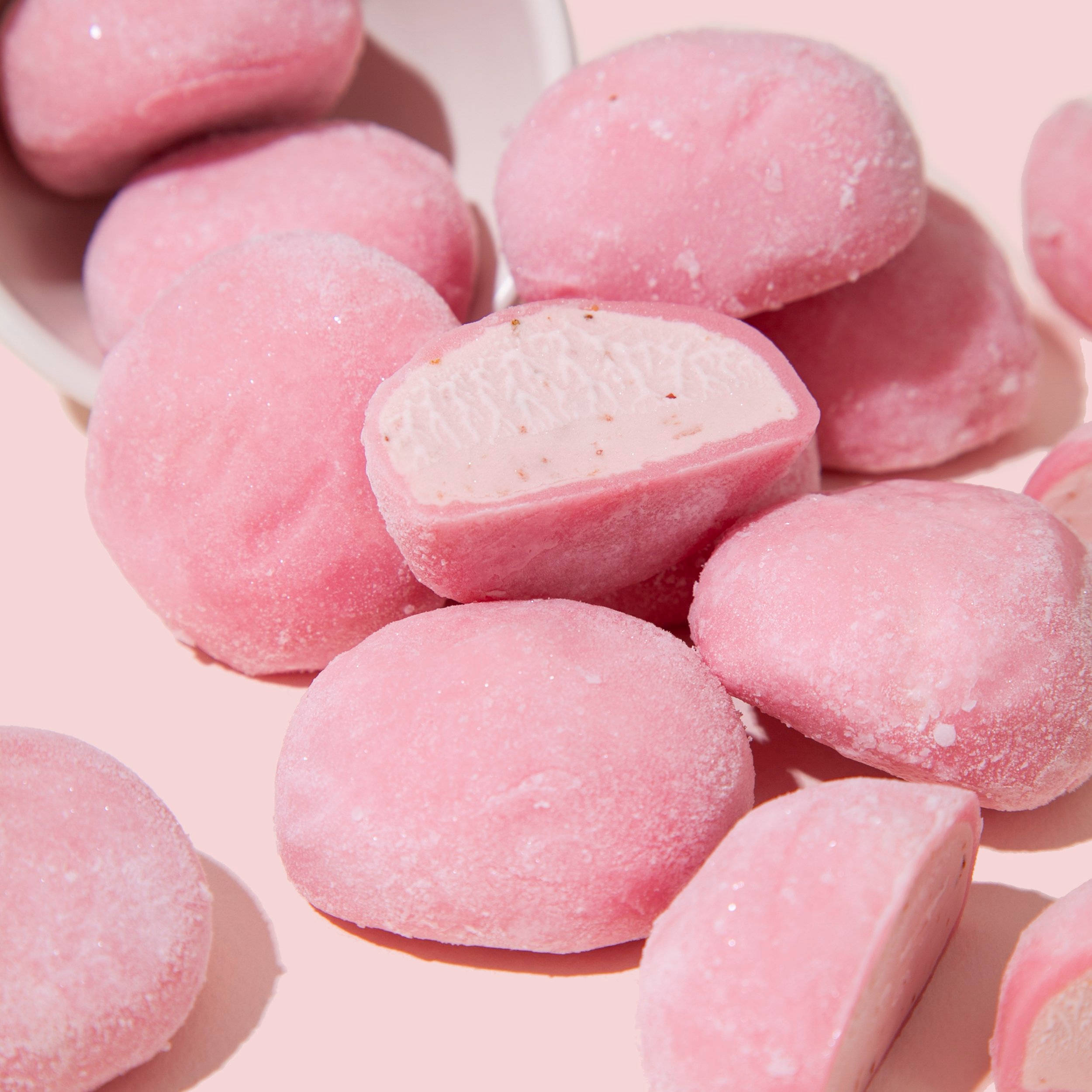 Mochi 桌布 壁紙 — 柔軟的粉紅色麻糬球，裹上糖粉，中心呈奶油白色，放在淺碗中，背景為粉彩粉紅色。