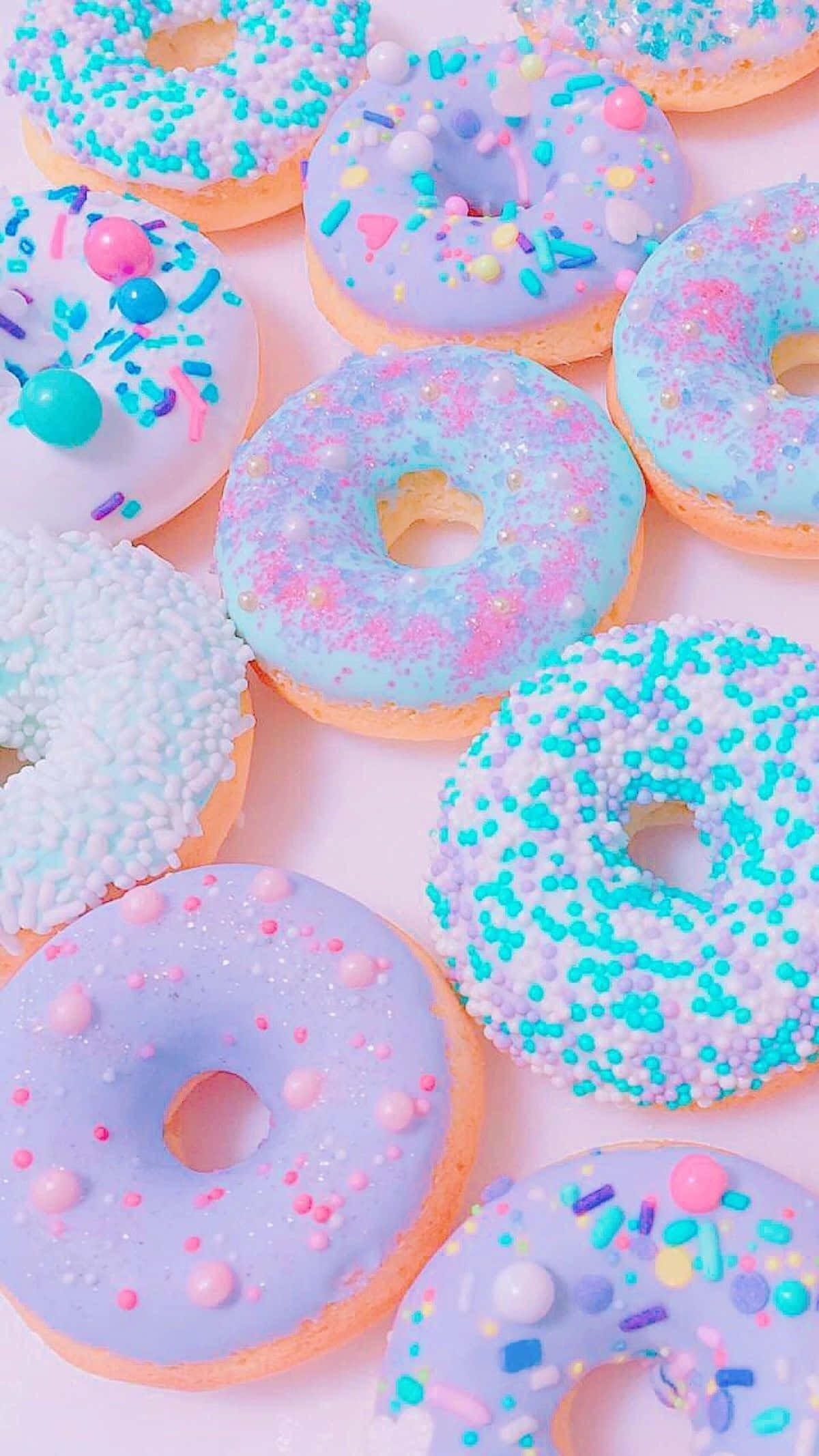 Cute Food iPhone 桌布 壁紙 — 柔軟粉紅色背景上擺放著色彩繽紛糖霜的柔和色調甜甜圈近距離特寫。