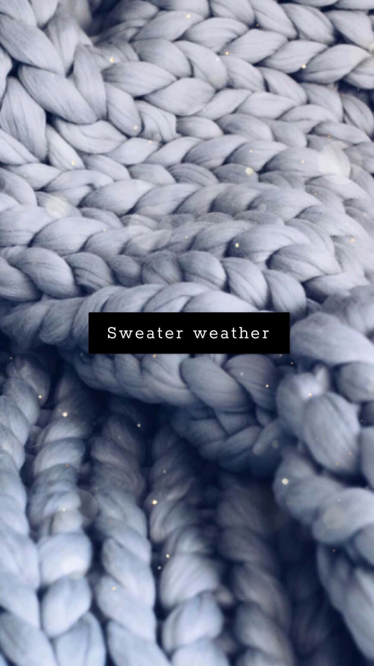 clothing 桌布 壁紙 — 柔軟藍灰色粗針織布料的特寫，帶有微妙的閃粉點綴和「Sweater weather」文字疊加。