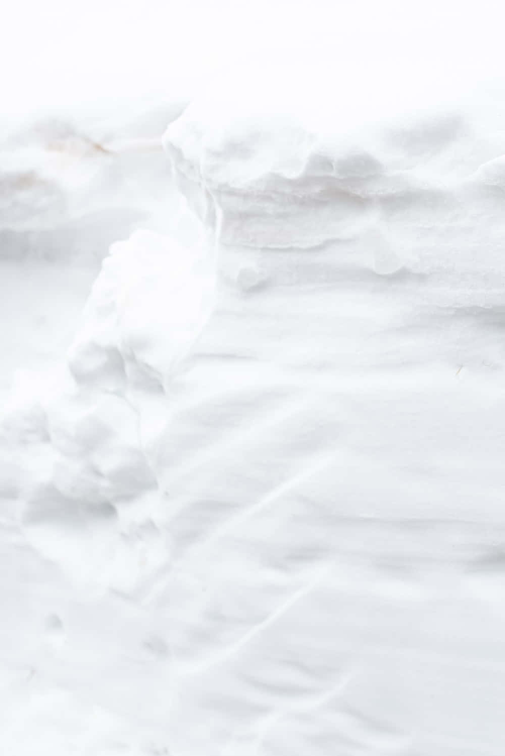 White iPhone 桌布 壁紙 — 柔軟質感的白色雪堆，帶有微妙的灰色和米色底色，營造出寧靜的冬日景觀。