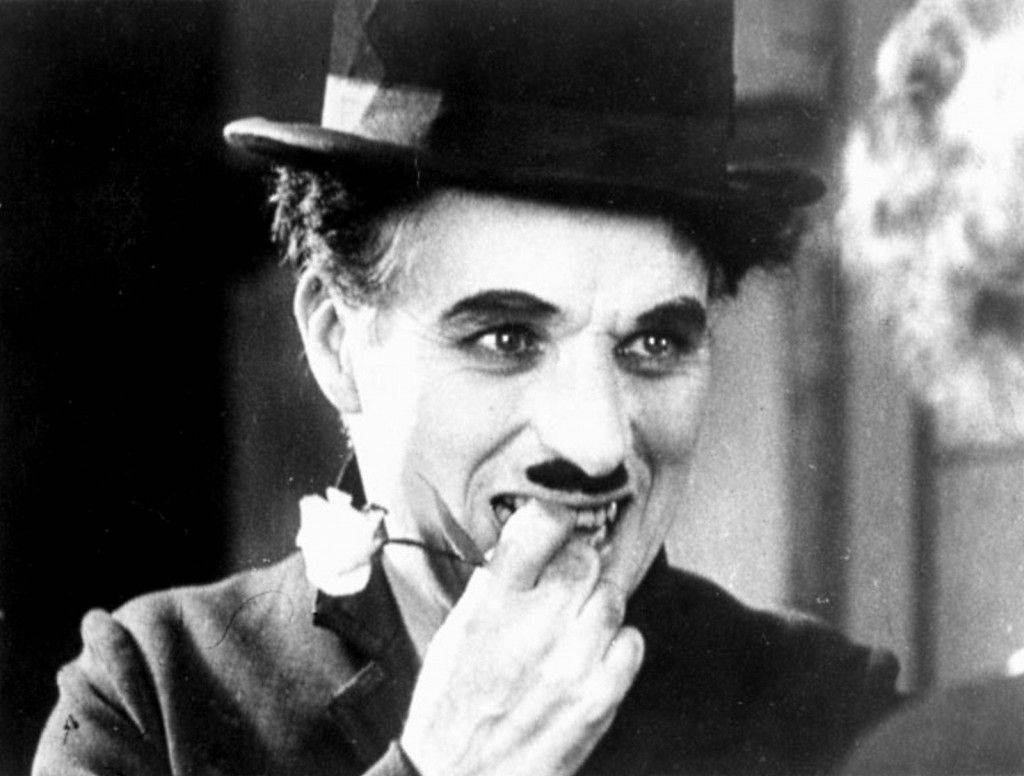 Chaplin 桌布 壁紙 — 查理·卓別林戴上標誌性的圓頂禮帽和鬍子，誇張地咬著一朵花，呈現經典黑白默片風格。