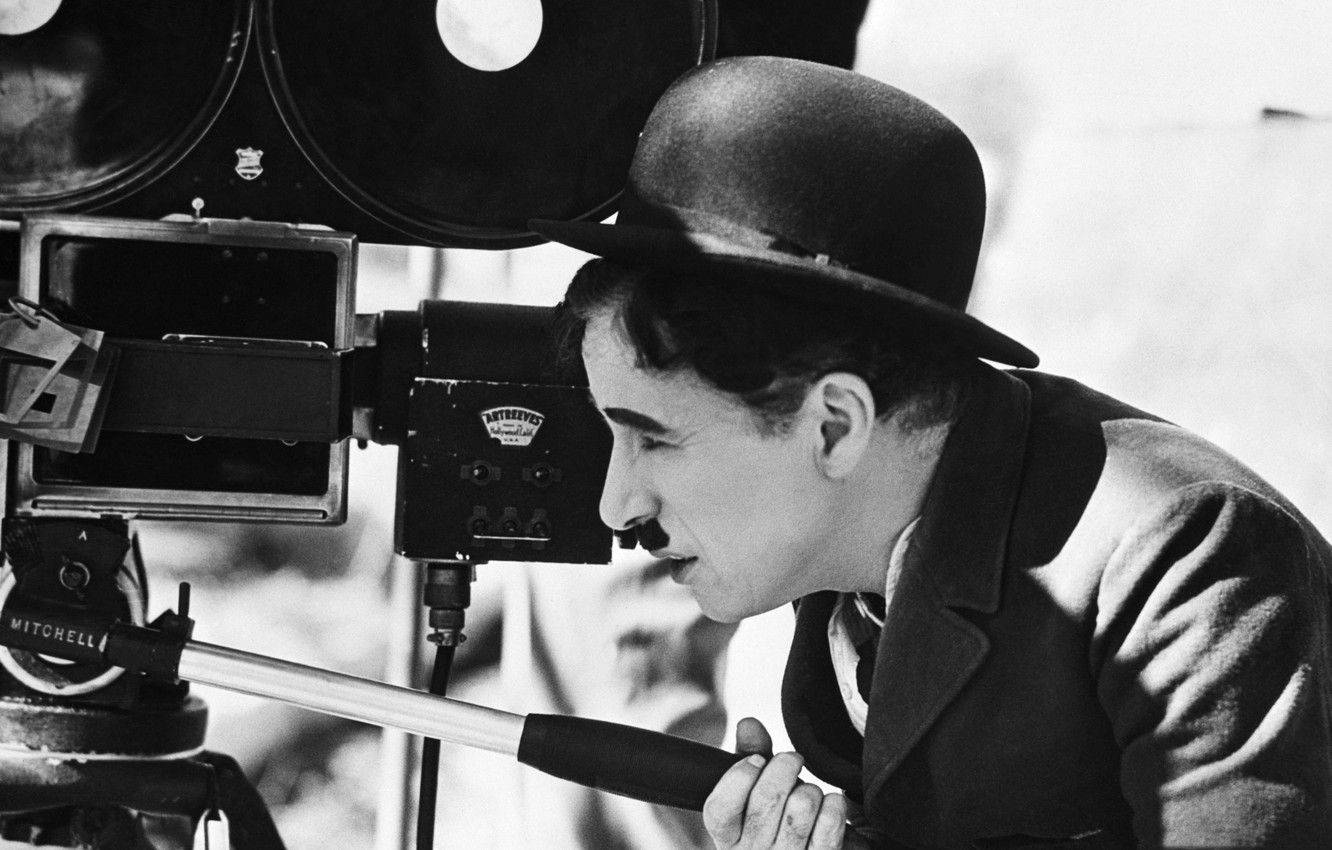 Chaplin 桌布 壁紙 — 查理·卓別林戴著他標誌性的圓頂禮帽和鬍子，透過復古的 Mitchell 相機鏡頭凝視。