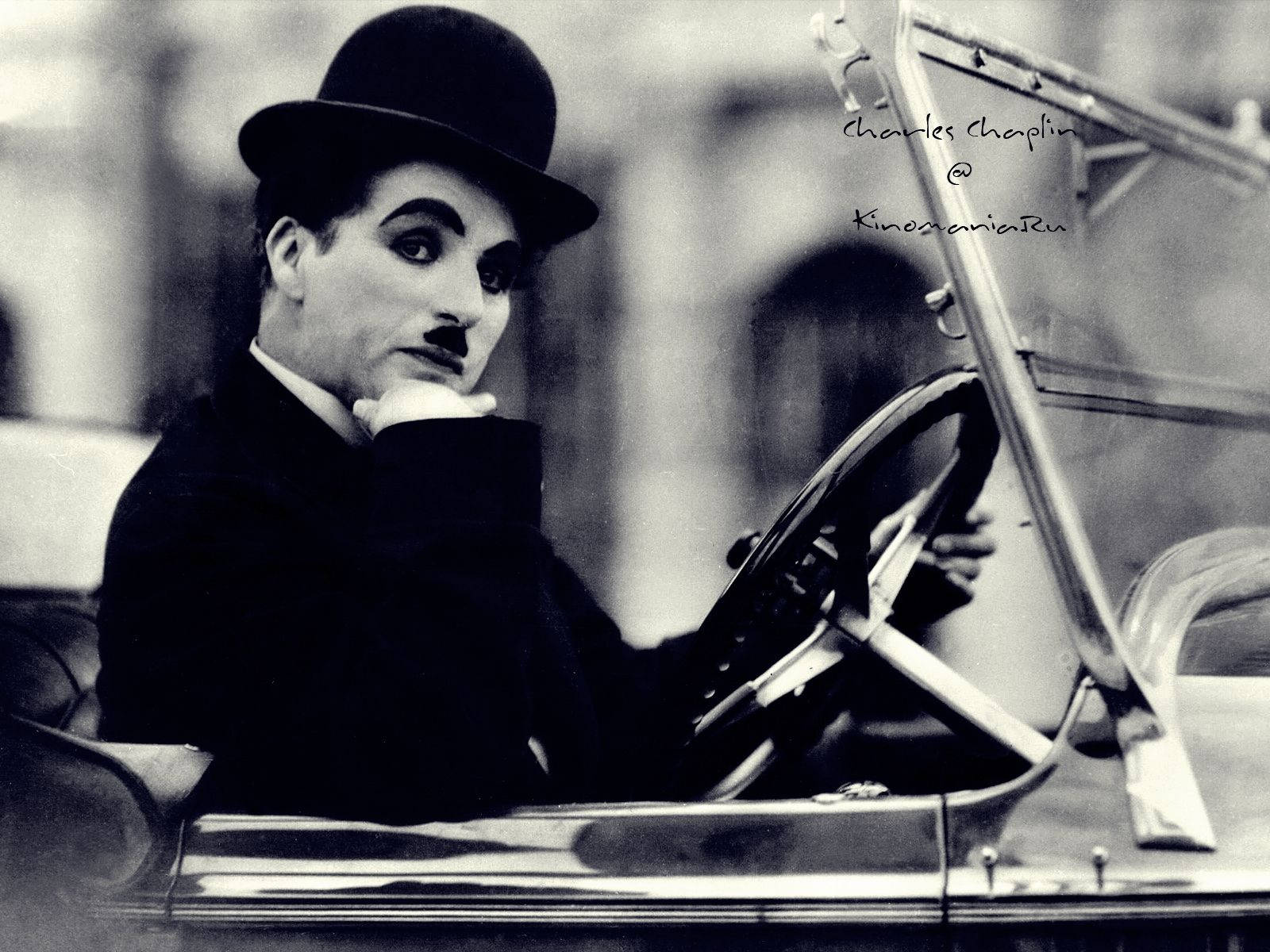 Chaplin 桌布 壁紙 — 查理·卓別林的經典黑白肖像，戴著標誌性的圓頂禮帽和鬍子，坐在一輛復古汽車中。