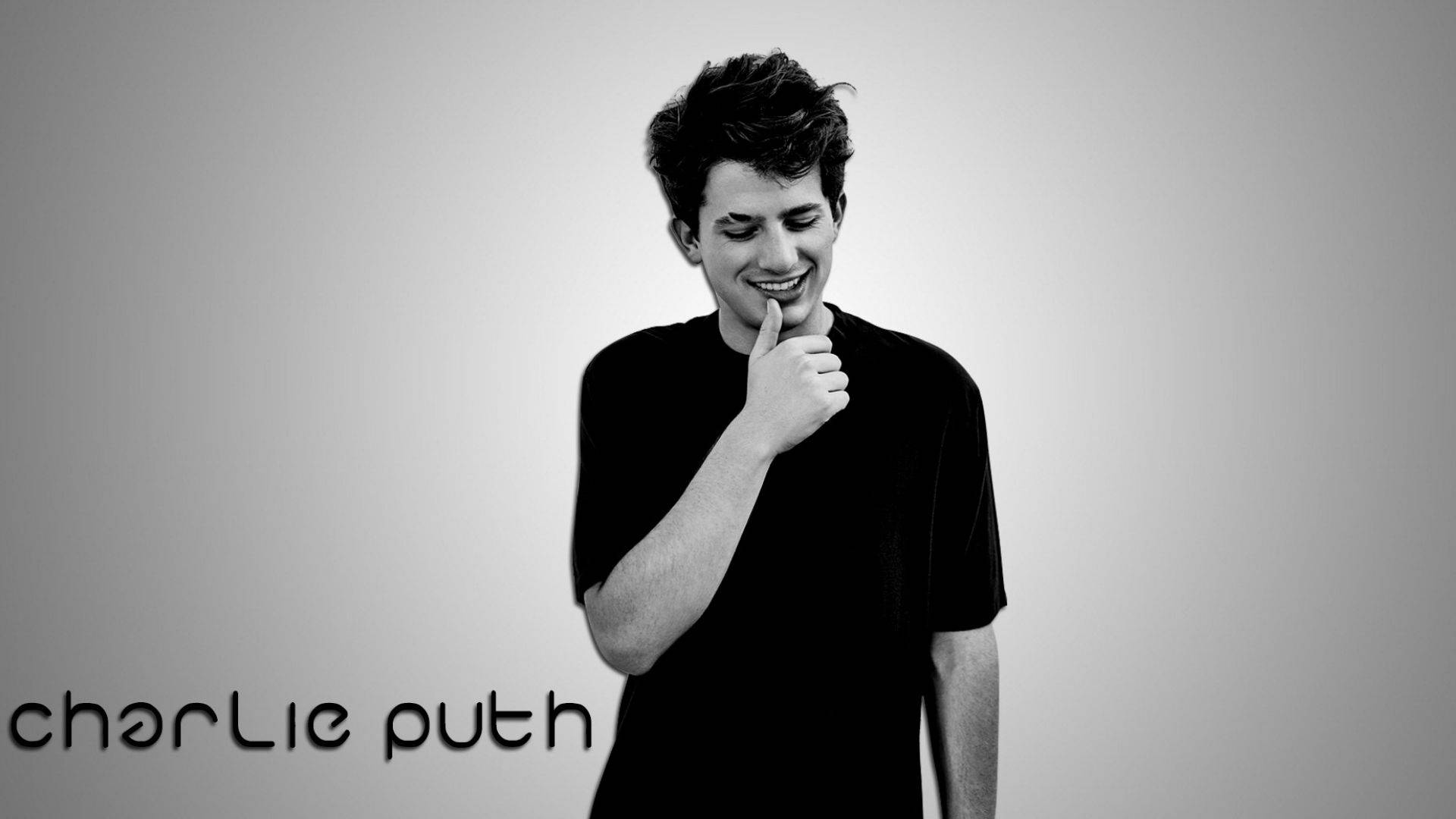 Charlie Puth 桌布 壁紙 — 查理·普斯（Charlie Puth）在純色漸變背景前微笑，手指放在嘴唇上的黑白肖像。
