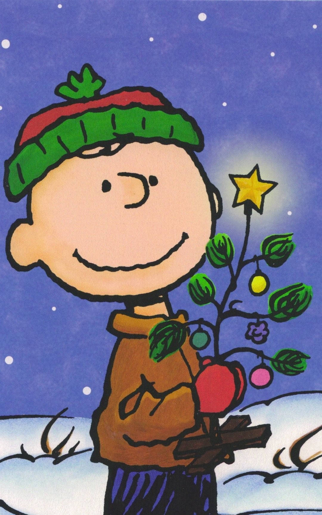 聖誕節 桌布 壁紙 — 查理布朗在雪花紛飛的星空下，溫暖地微笑著，手中拿著一棵裝飾好的小聖誕樹。