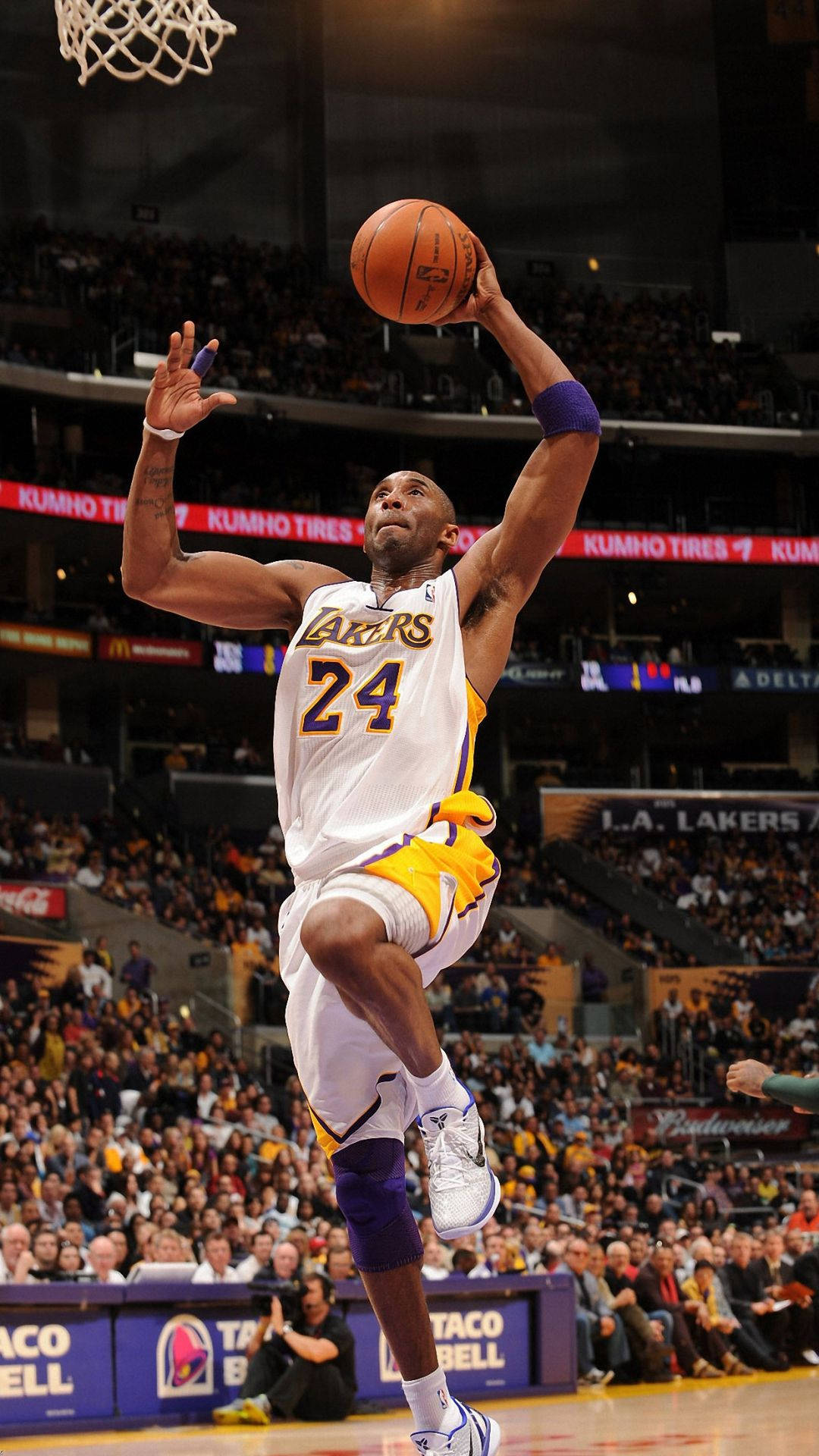 Kobe Bryant iPhone 桌布 壁紙 — 柯比·布萊恩身穿湖人球衣，在擠滿觀眾的場館內，於明亮的場館燈光下凌空灌籃。
