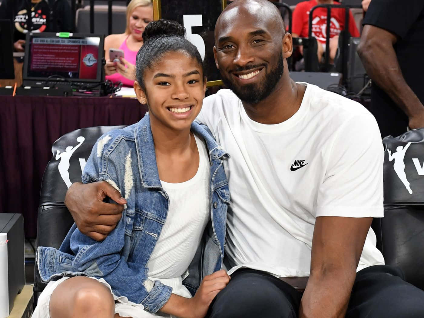 Kobe And Gigi 桌布 壁紙 — 柯比布萊恩與女兒吉安娜在籃球場座位上溫暖微笑，兩人都散發著喜悅和聯繫。