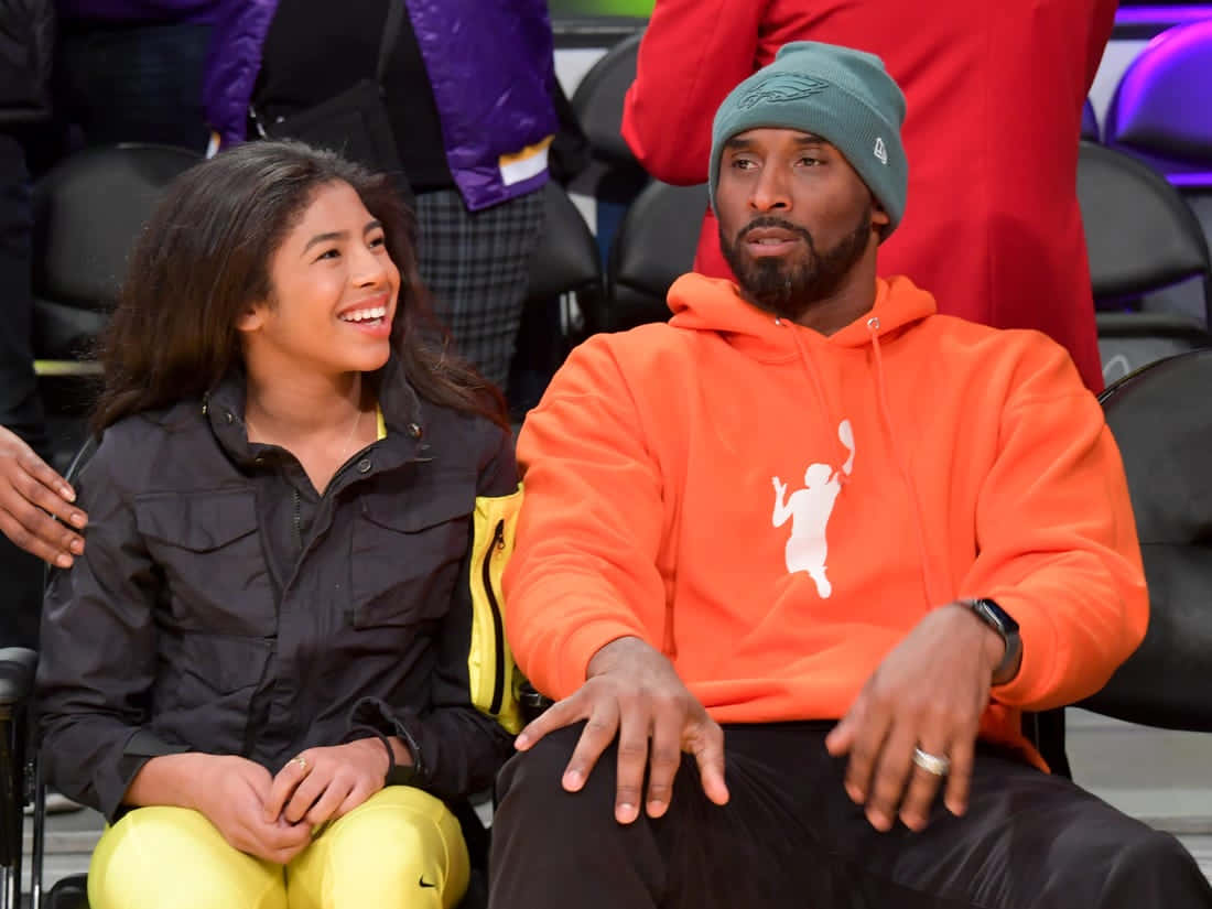 Kobe And Gigi 桌布 壁紙 — 柯比布萊恩與女兒吉安娜在籃球比賽中穿著鮮豔的橙色和黃色服裝一起微笑。