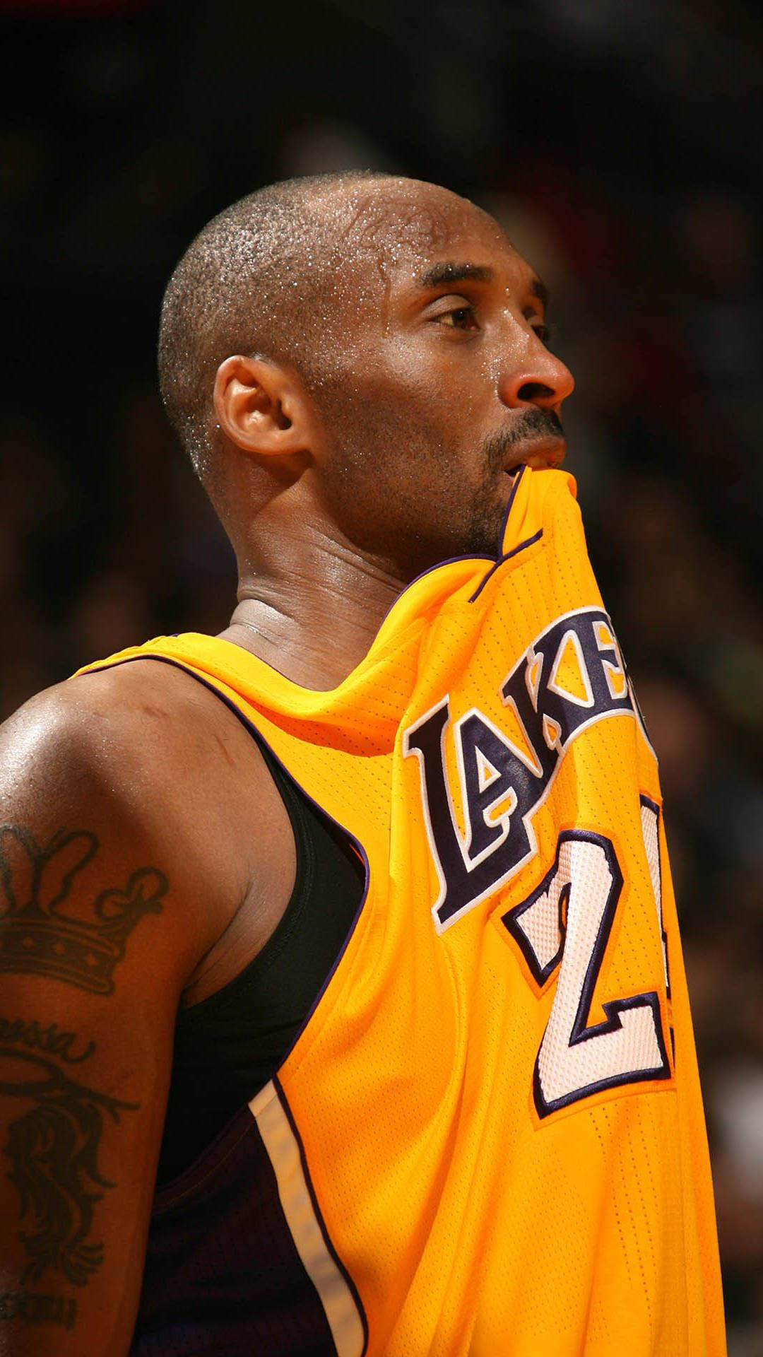 Kobe Bryant iPhone 桌布 壁紙 — 柯比布萊恩身穿湖人球衣，在場館燈光下激烈的籃球比賽中咬住袖子。