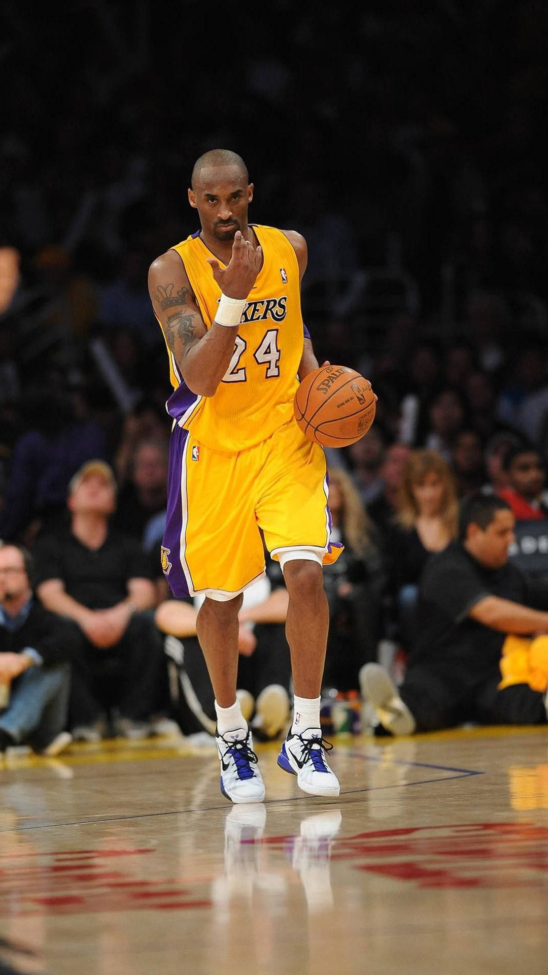NBA iPhone 桌布 壁紙 — 柯比布萊恩身穿黃色湖人球衣，在拋光球場上運球，背景是模糊的人群。
