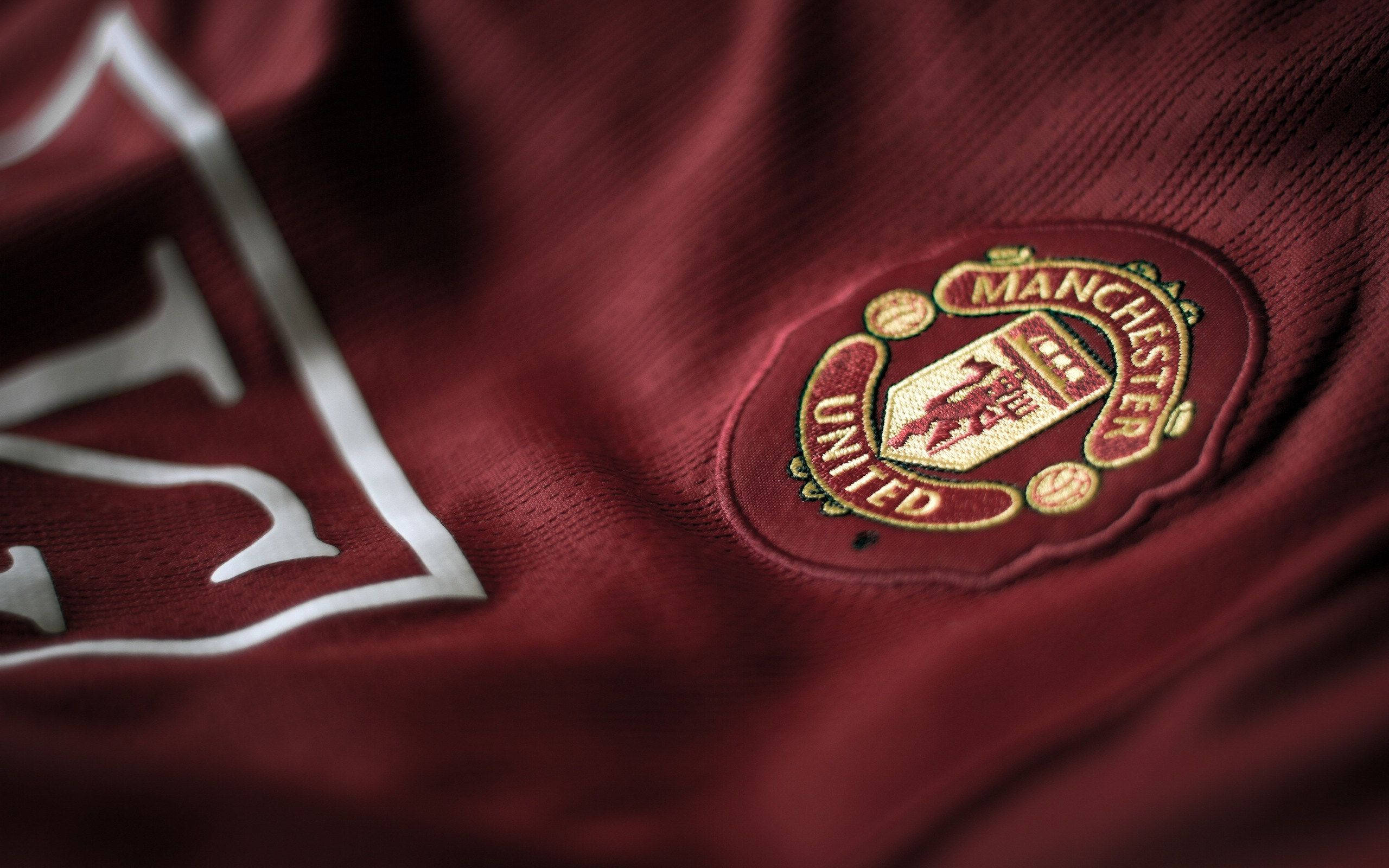 Manchester United Logo 桌布 壁紙 — 栗色曼聯足球球衣特寫，帶有刺繡會徽和白色贊助商標誌。