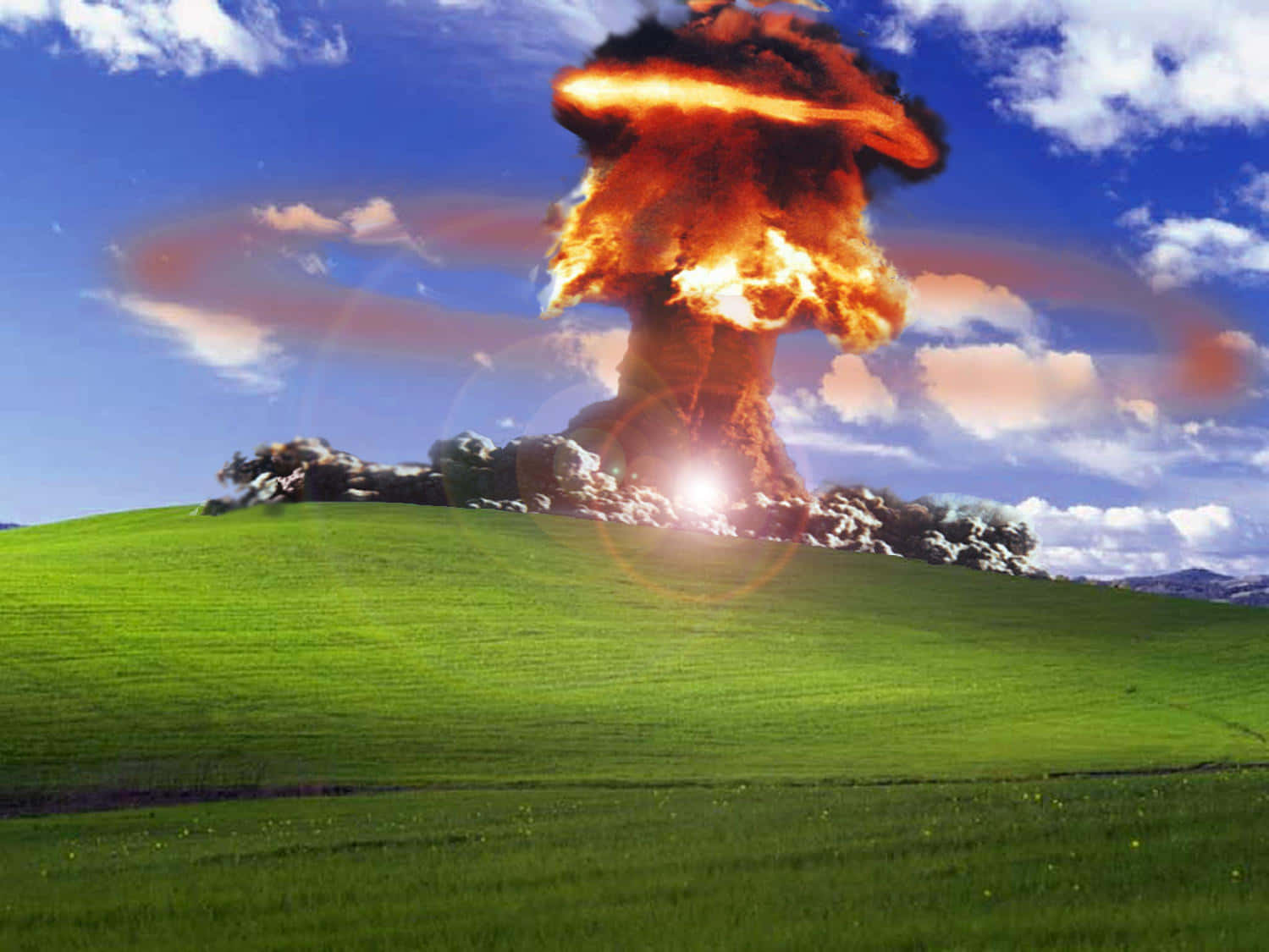 Windows XP 桌布 壁紙 — 核爆炸在茂密的綠色山丘頂上爆發，背景是明亮的藍天和蓬鬆的白雲。