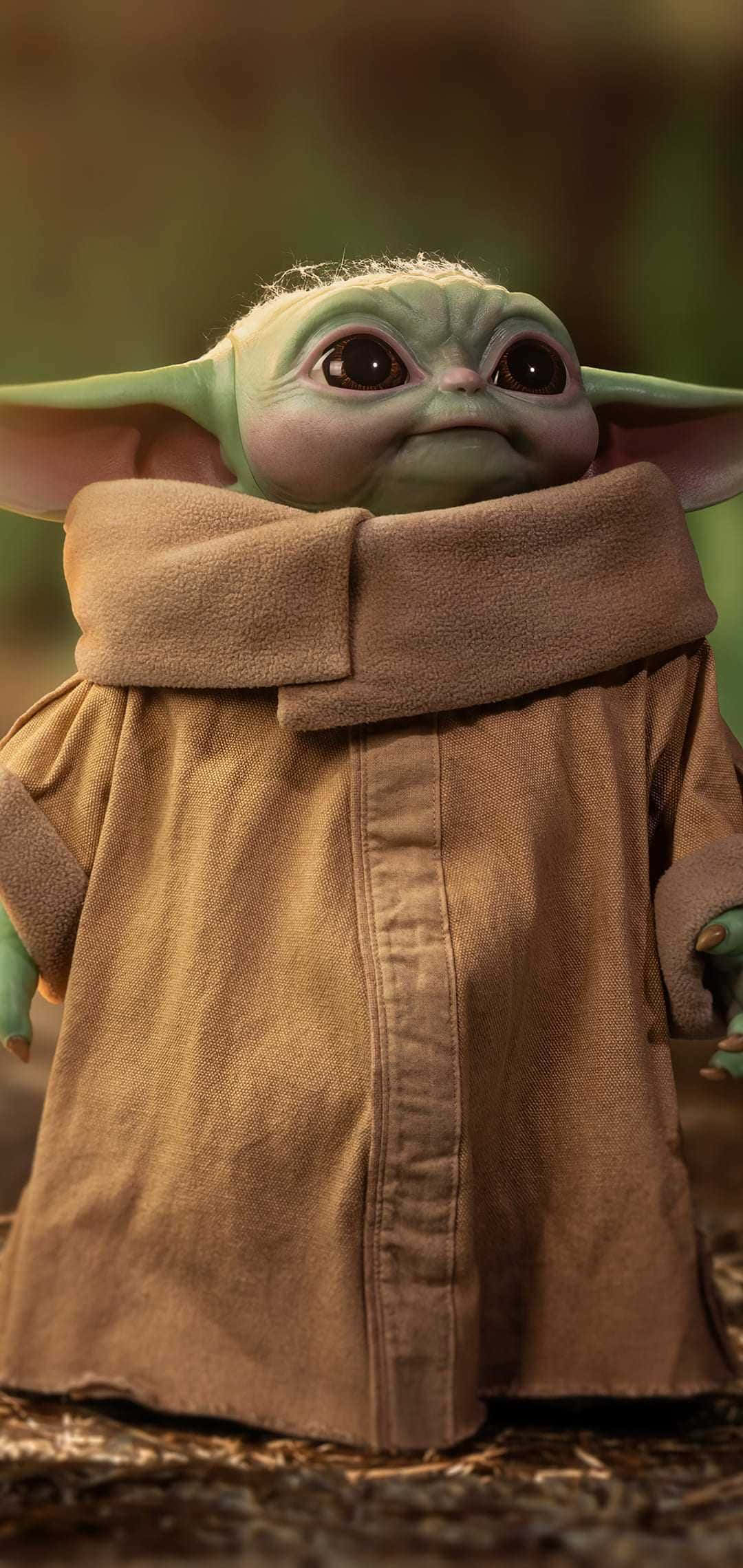 Baby Yoda iPhone 桌布 壁紙 — 格羅古（Grogu）的特寫，綠色眼睛的嬰兒尤達，身穿棕色長袍，柔和燈光與模糊的森林背景。