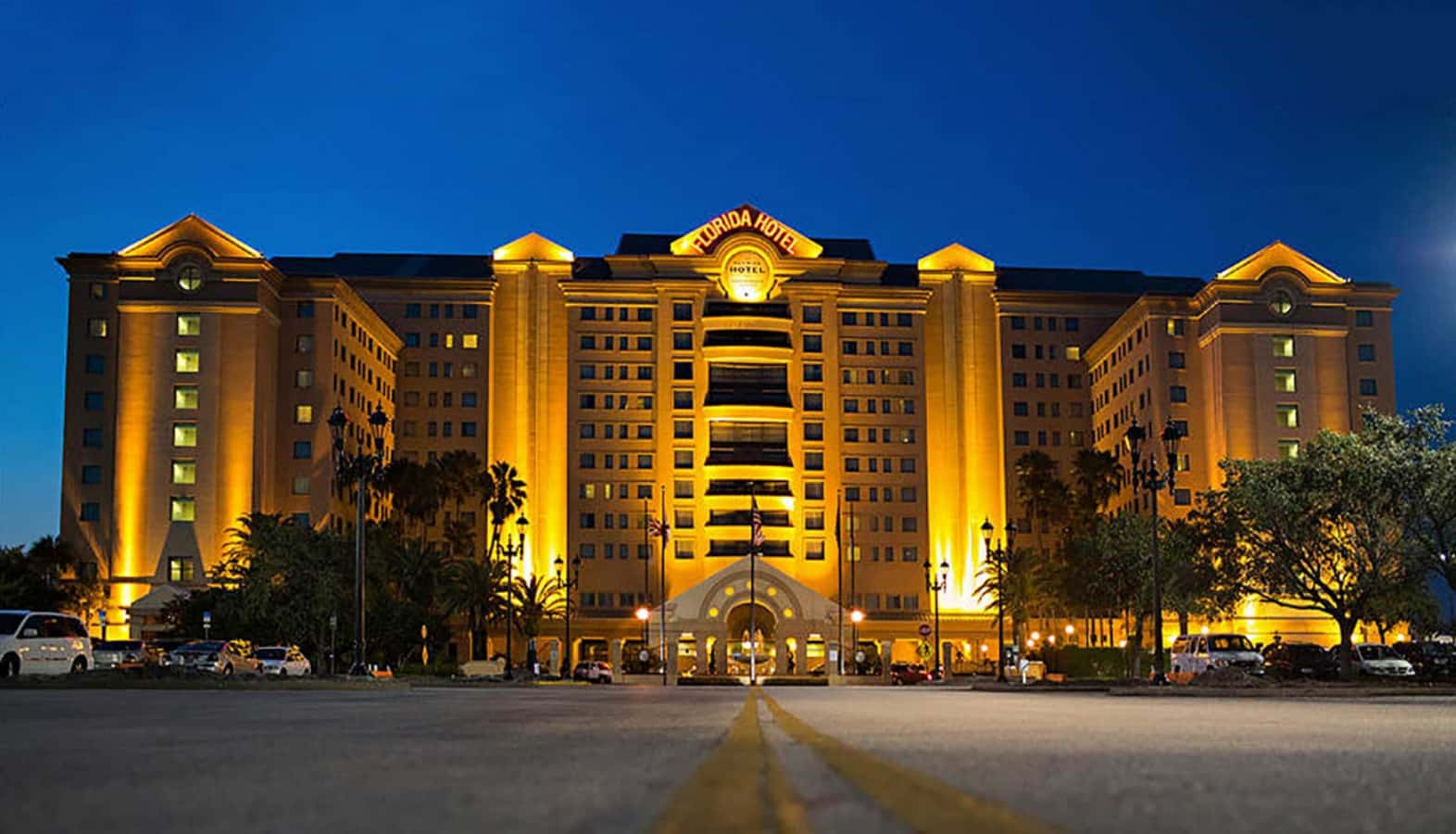 Hotel 桌布 壁紙 — 格蘭佛羅里達酒店在溫暖的金色燈光下，映襯著深藍色的暮色天空，棕櫚樹和停放的汽車。