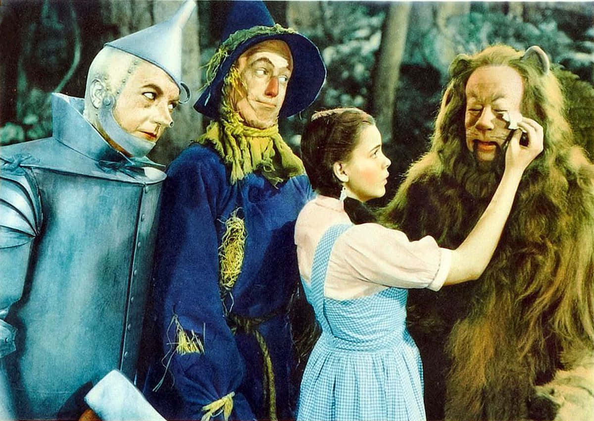 wizard of oz 桌布 壁紙 — 桃樂絲溫柔地擦去獅子的眼淚，而錫人與稻草人在茂密的森林場景中觀看。