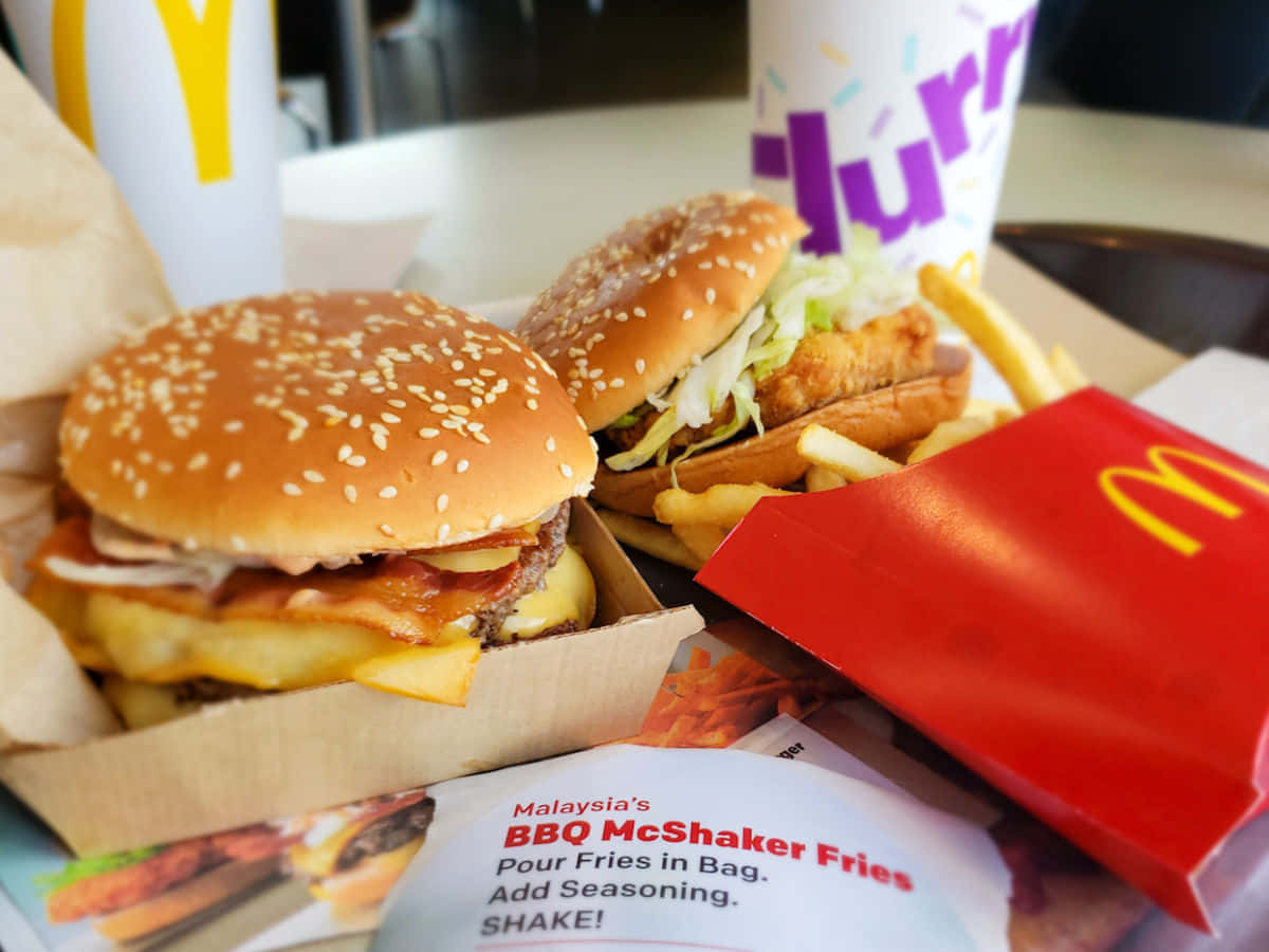 Mcdonald's Food 桌布 壁紙 — 桌上兩個麥當勞漢堡和薯條的特寫，附有品牌包裝。