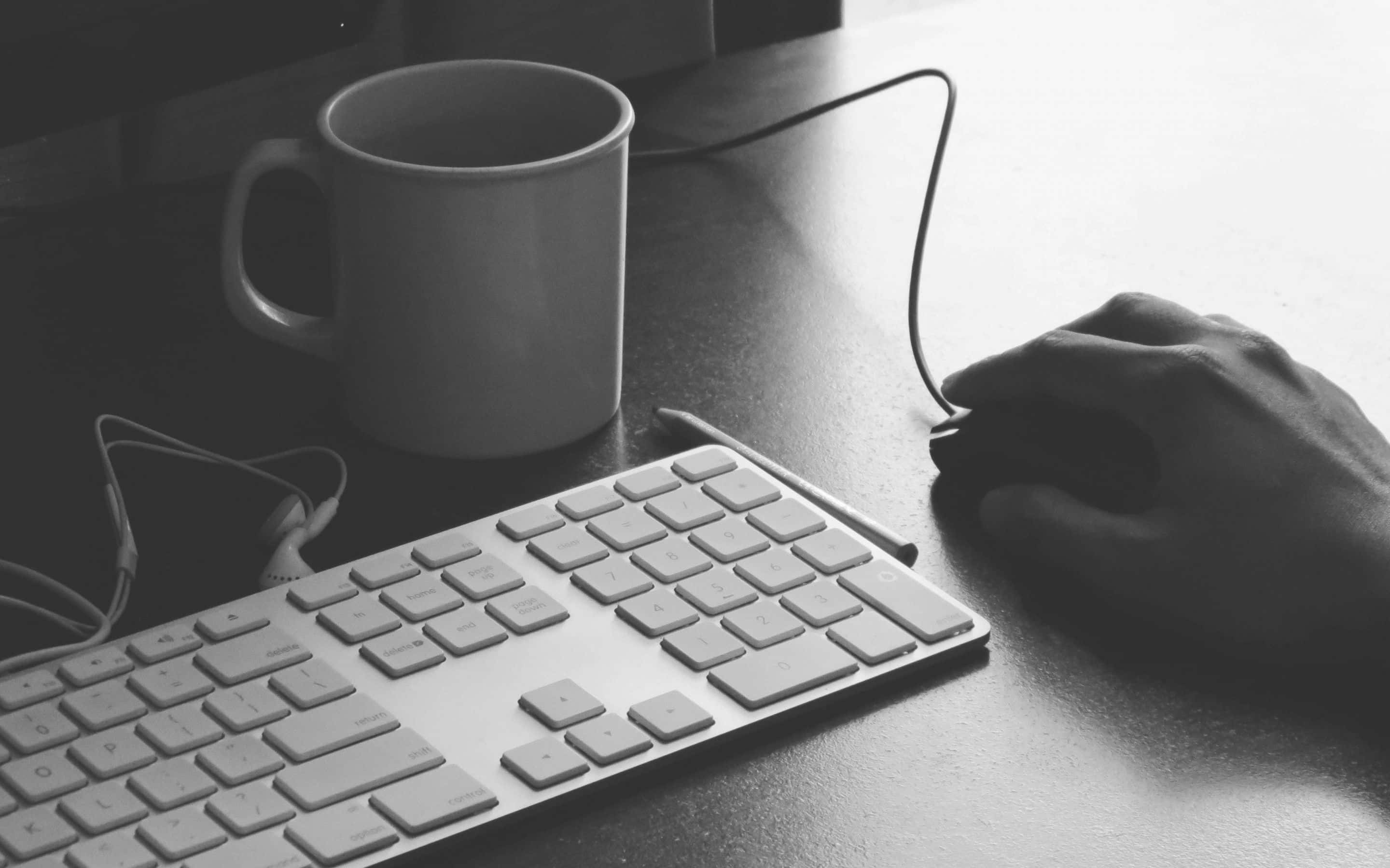 Best Office 桌布 壁紙 — 桌上鍵盤和咖啡杯旁使用滑鼠的手部單色特寫。
