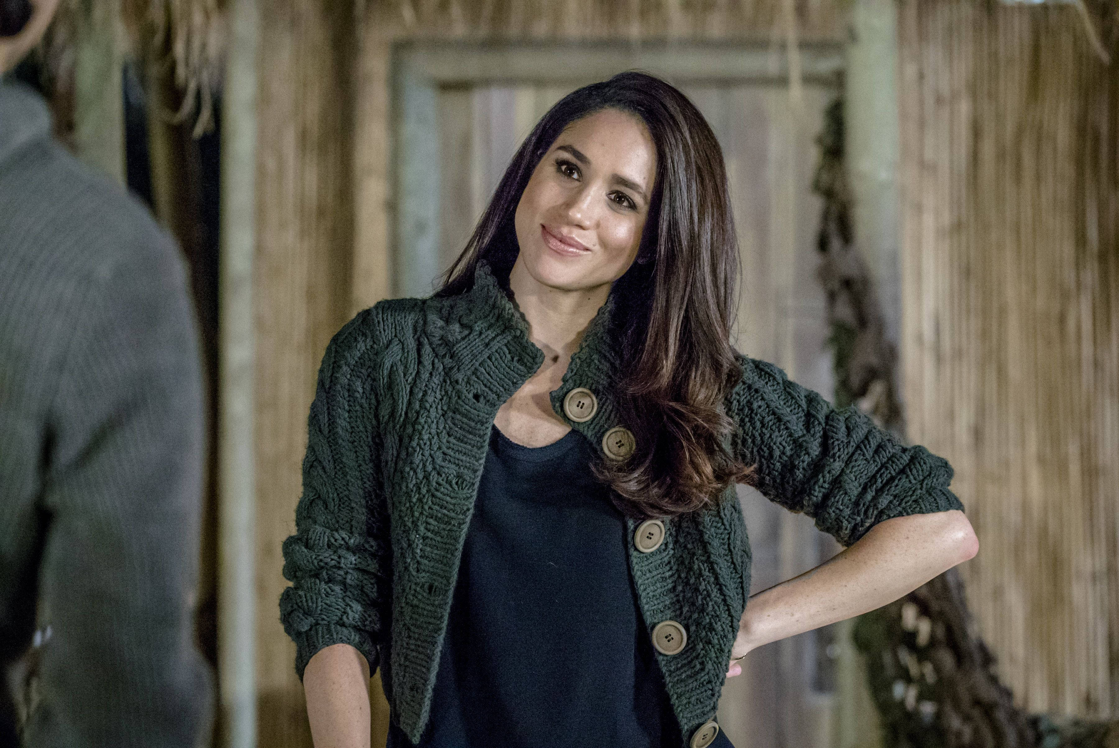 Meghan Markle 桌布 壁紙 — 梅根·馬克爾穿著質感綠色開襟毛衣，在質樸的竹製背景下溫暖微笑。
