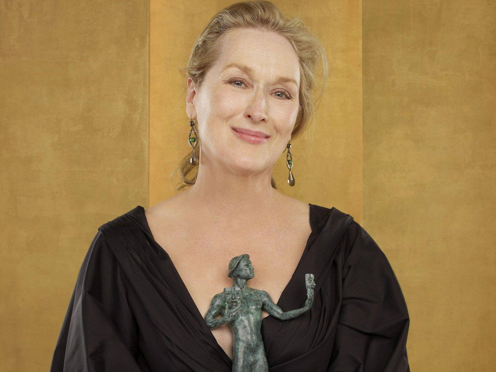 Meryl Streep 桌布 壁紙 — 梅莉·史翠普在金色紋理背景前溫暖微笑，手持一座銅像。