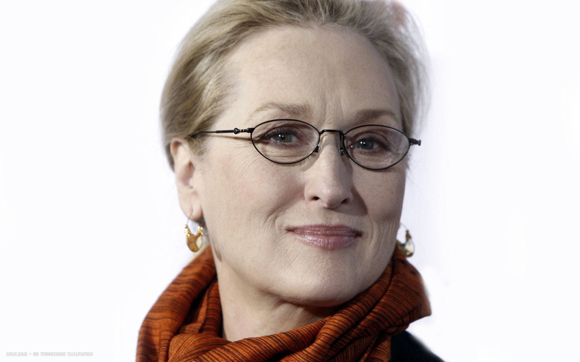 Meryl Streep 桌布 壁紙 — 梅莉·史翠普戴著眼鏡和鏽色圍巾，在純白背景下溫暖地微笑。