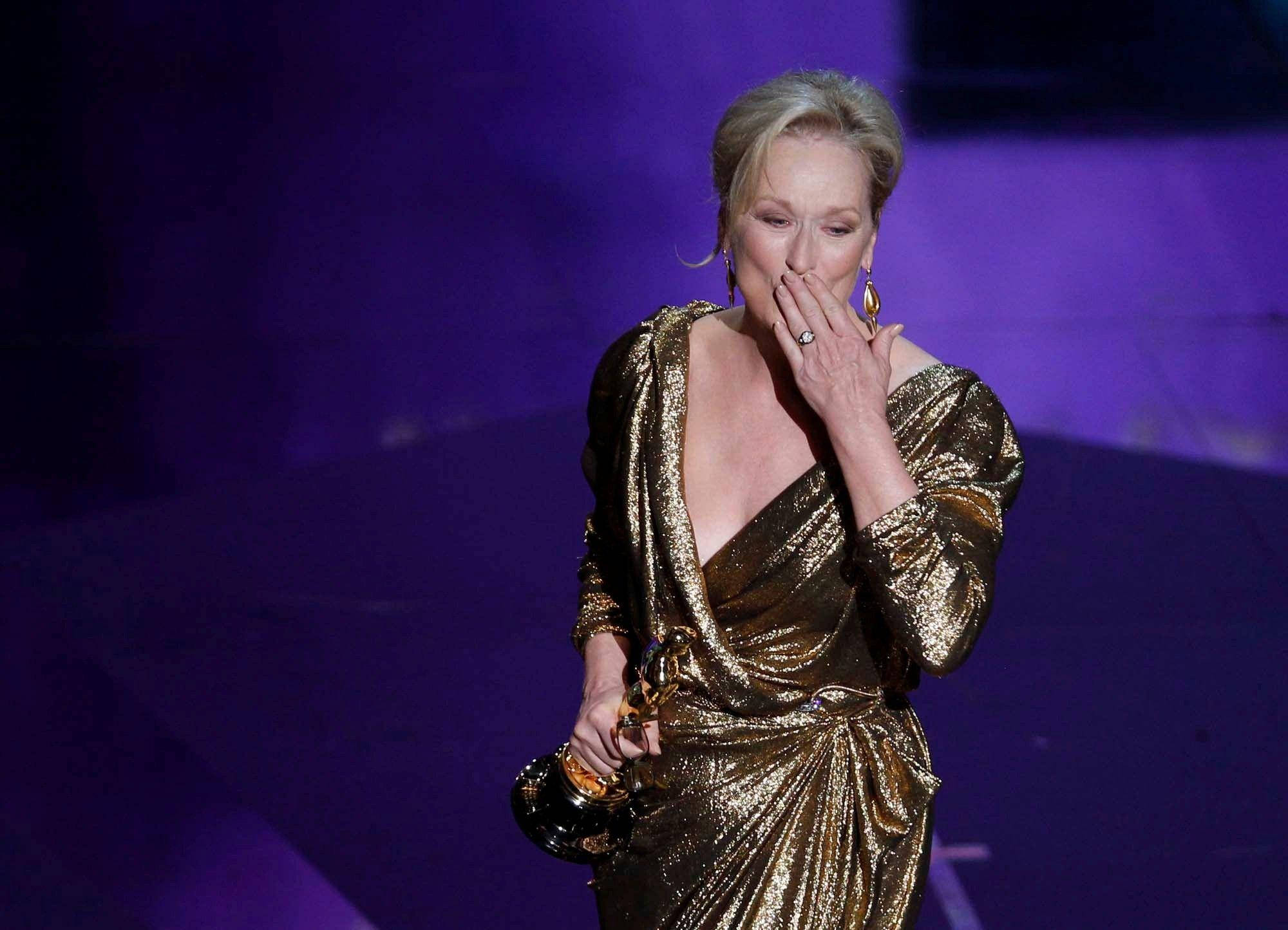 Meryl Streep 桌布 壁紙 — 梅莉·史翠普身穿閃閃發光的金色長袍，在紫色燈光的舞台上拿著奧斯卡獎，情感難以置信地捂住嘴巴。
