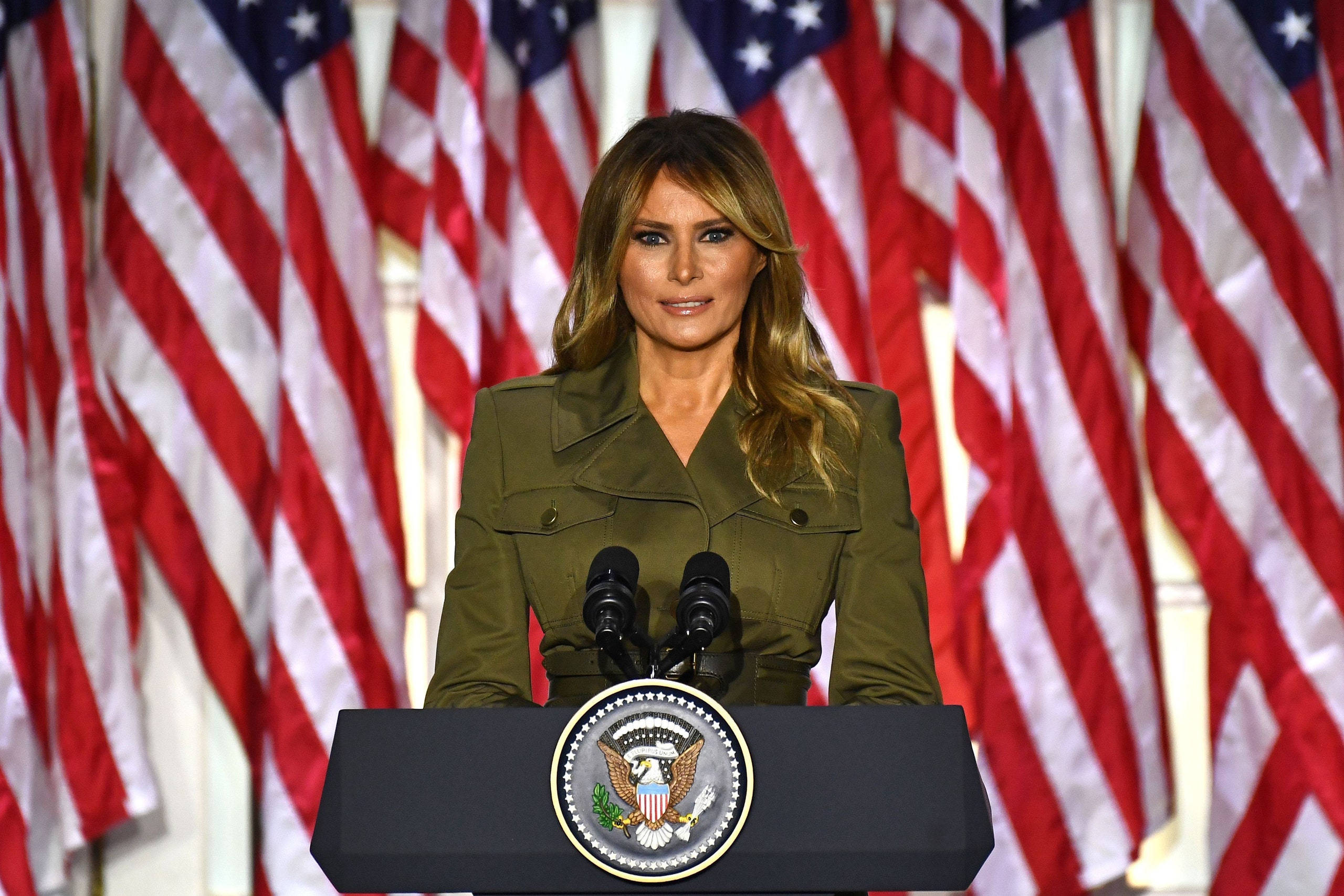 Melania 桌布 壁紙 — 梅蘭妮亞·川普站在總統講台上，身後有美國國旗，在正式場合中。