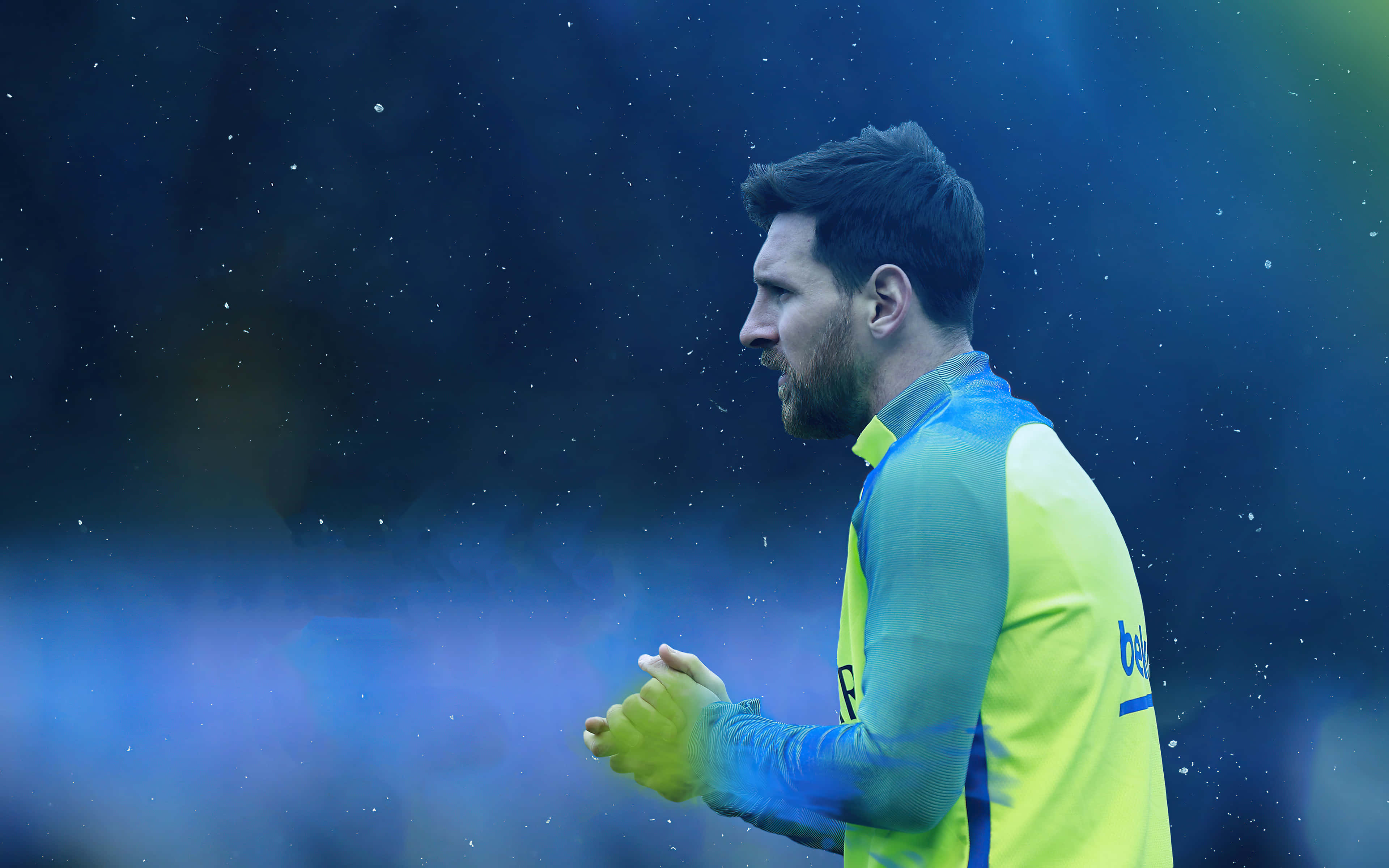 Messi Cool 桌布 壁紙 — 梅西身穿亮黃色訓練球衣，在模糊的藍色球場背景下拍手，雪花飄落。