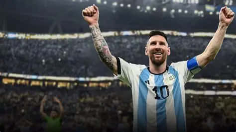 Messi 壁紙 — 梅西身穿阿根廷球衣，在明亮的燈光下於座無虛席的球場中高舉拳頭慶祝勝利。