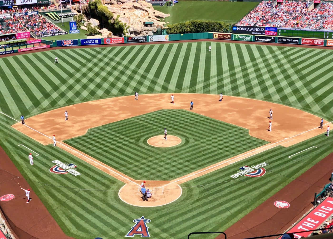 Baseball Field 桌布 壁紙 — 棒球場的鳥瞰圖，球員在精心條紋的綠色和棕色場地上，在明亮的日光下比賽。