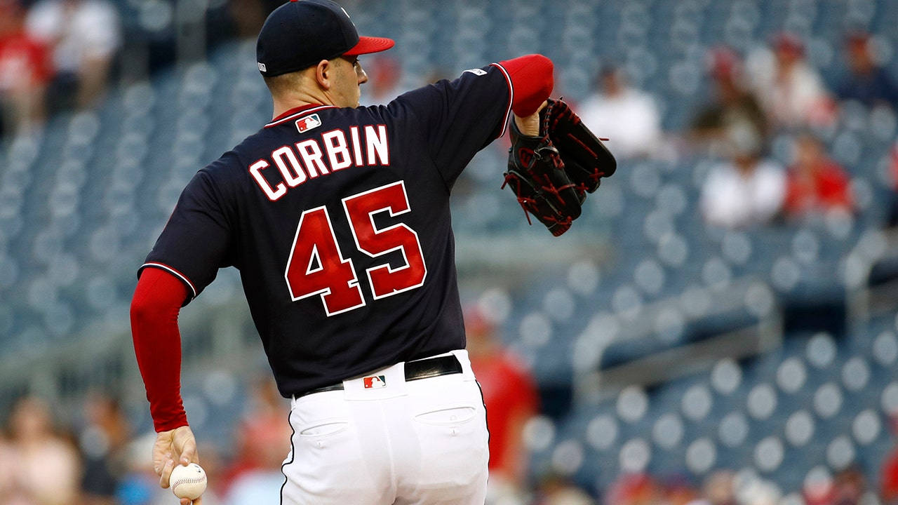 運動 桌布 壁紙 — 棒球投手 Corbin 身穿海軍藍球衣 45 號，在陽光明媚的日子裡，在觀眾稀疏的球場上準備投球。