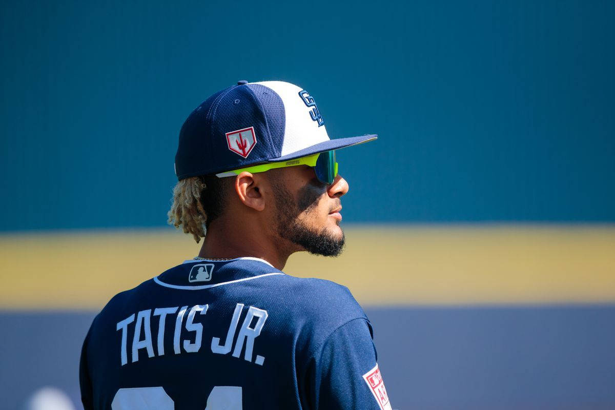 Tatis 桌布 壁紙 — 棒球運動員 Fernando Tatis Jr. 身穿海軍藍制服和螢光綠色太陽眼鏡，側身站在藍黃色牆壁前。