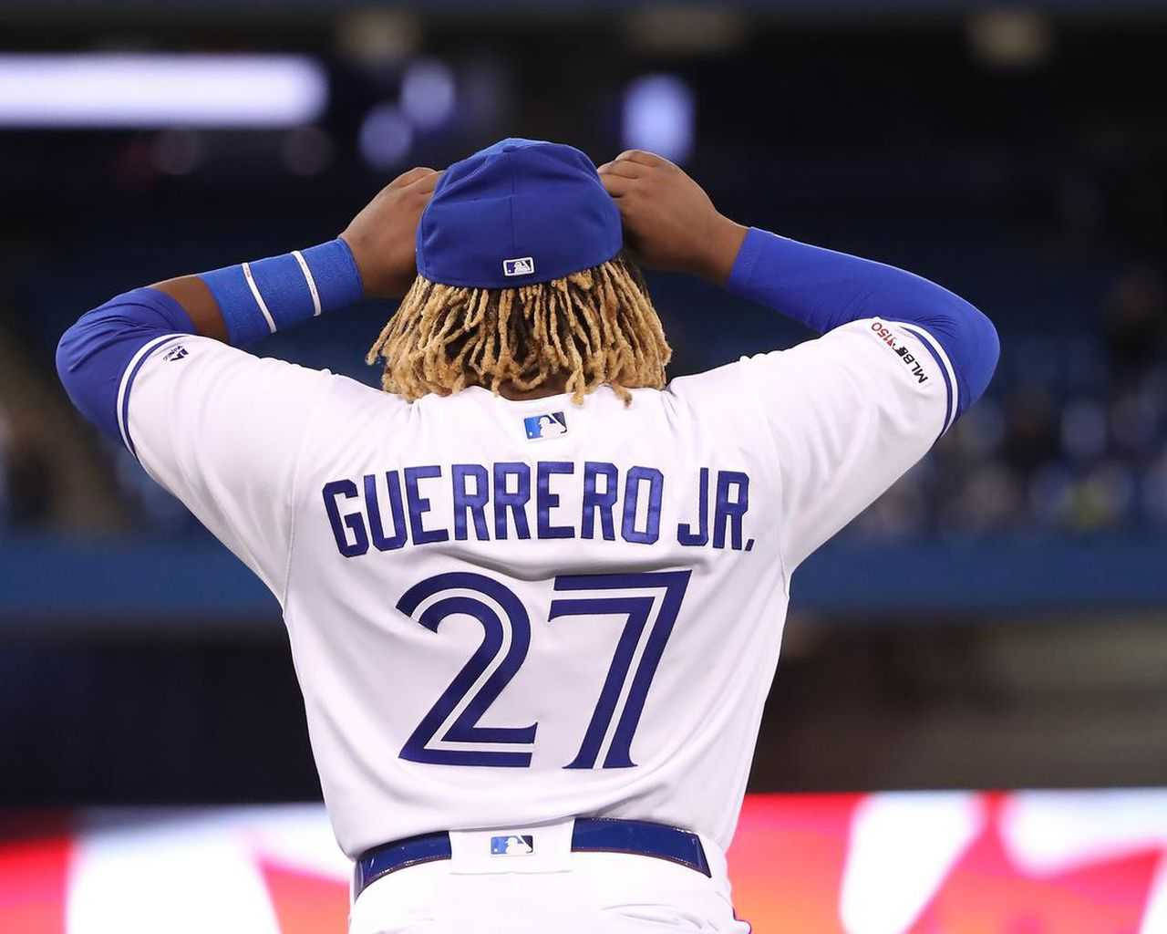 Vladimir 桌布 壁紙 — 棒球選手 Guerrero Jr. 從背後調整他的帽子，站在燈光明亮的球場上。