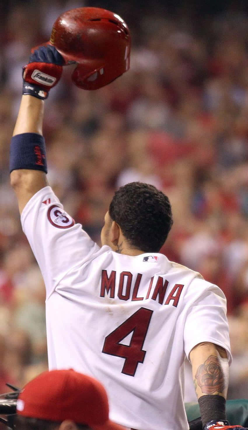 Yadier Molina 桌布 壁紙 — 棒球選手 Molina 4號在球場上高舉紅色頭盔，向歡呼的球迷展示勝利。