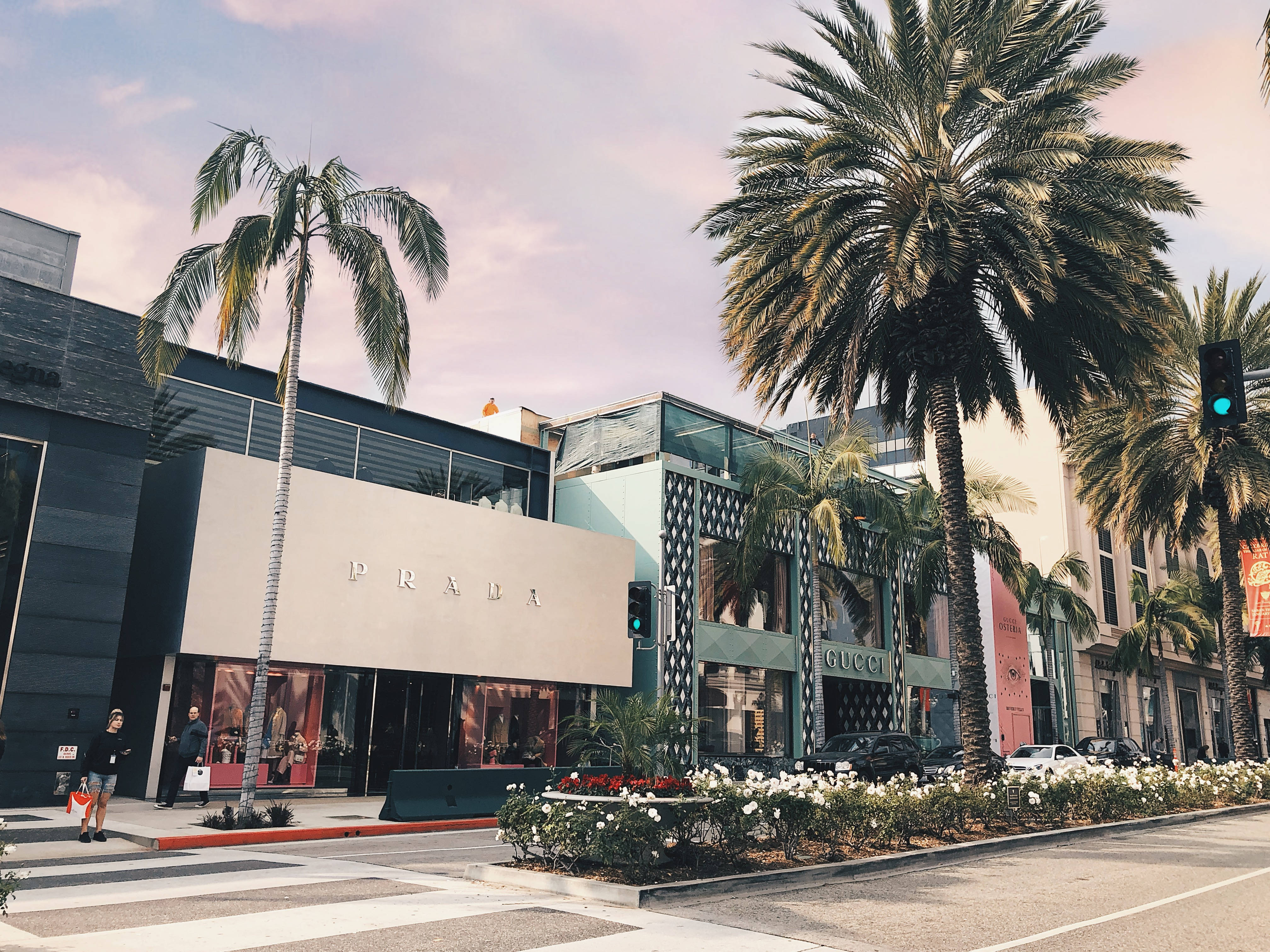Prada 桌布 壁紙 — 棕櫚樹排列在一條時尚的街道上，Prada 和 Gucci 商店在柔和的暮色天空下。
