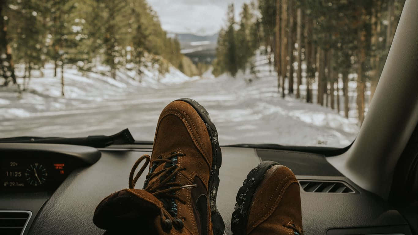 棕色登山靴擱在汽車儀表板上，面向一條積雪的森林道路。 — 鞋子 GIF 壁紙