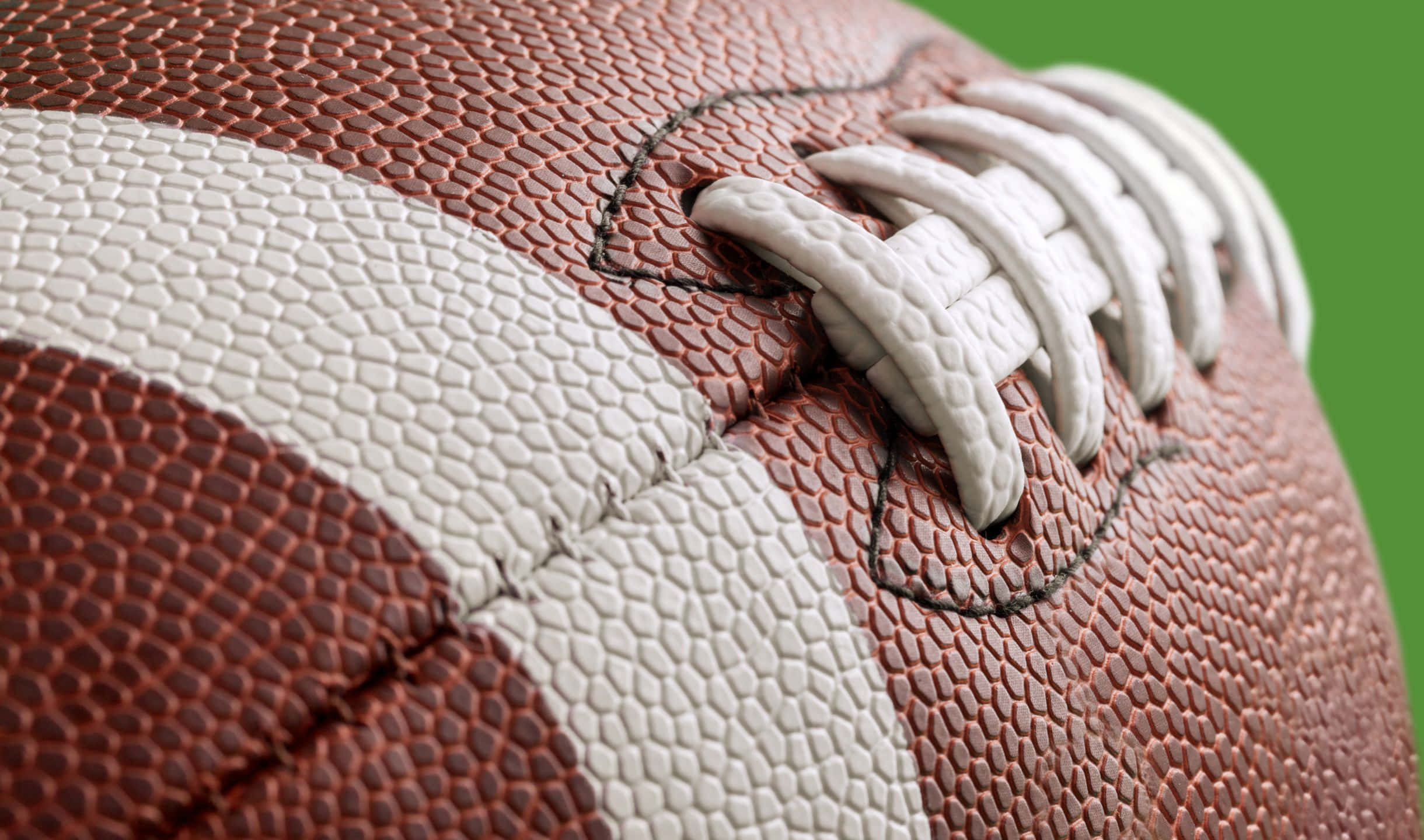 2440x1440 Football 桌布 壁紙 — 棕色皮革美式足球的特寫，帶有白色鞋帶和條紋，背景為充滿活力的綠色。