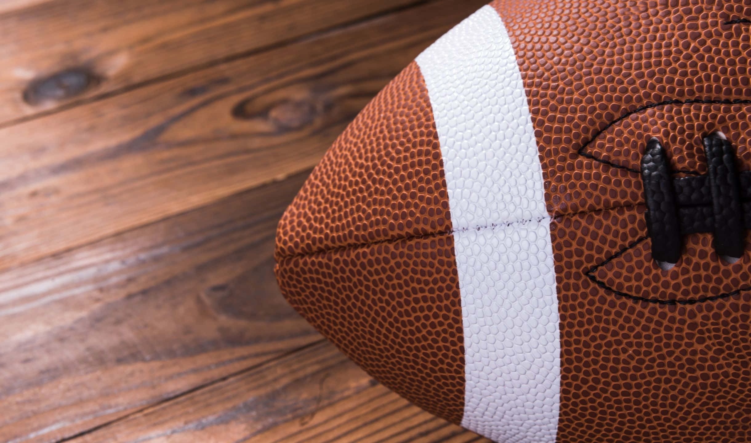 2440x1440 Football 桌布 壁紙 — 棕色皮革美式足球近距離特寫，帶有白色條紋，放置在質樸的木質表面上。