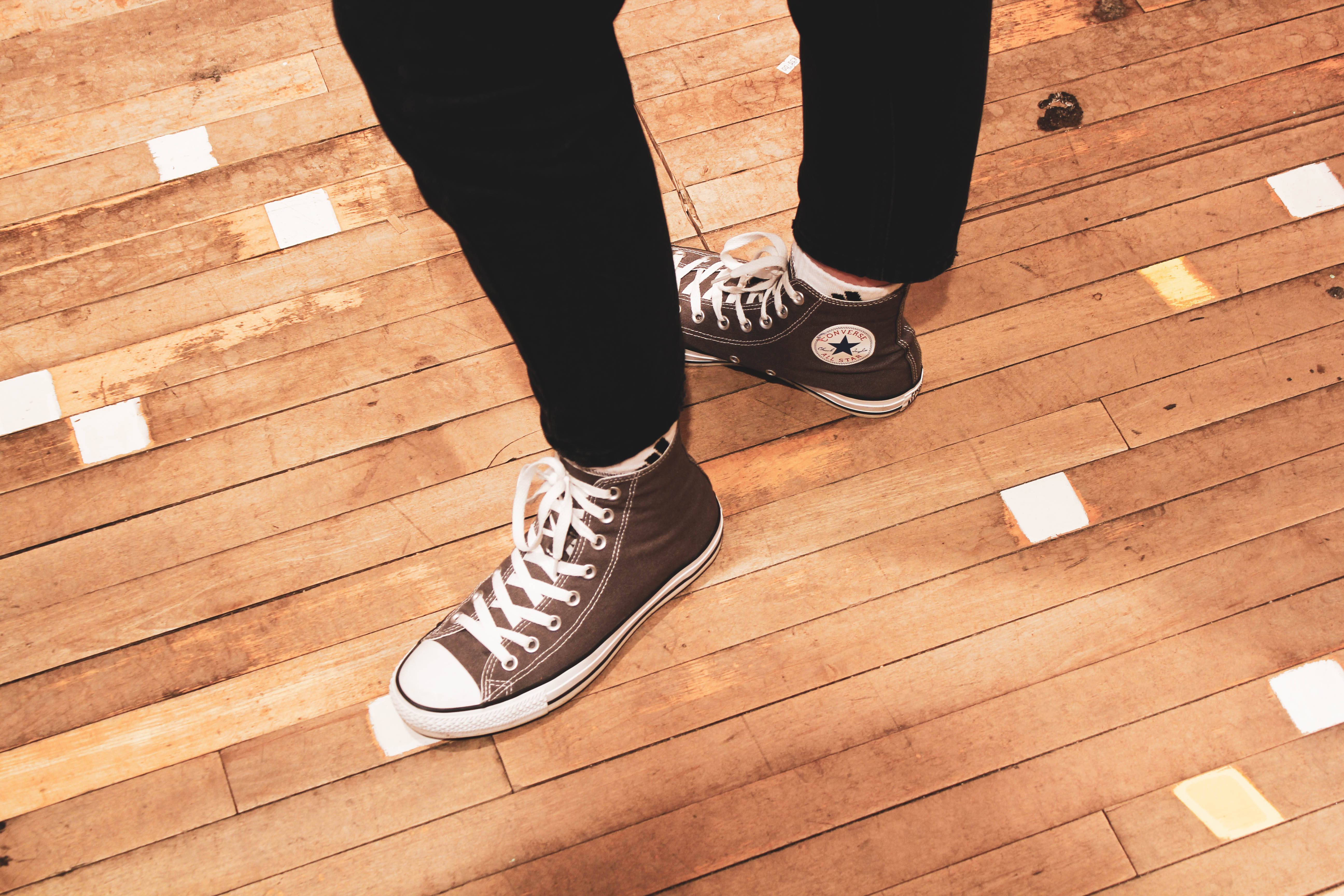 Converse 桌布 壁紙 — 棕色高筒運動鞋特寫，白色鞋帶和星星標誌，放在磨損的木地板上，散落著白色斑點。