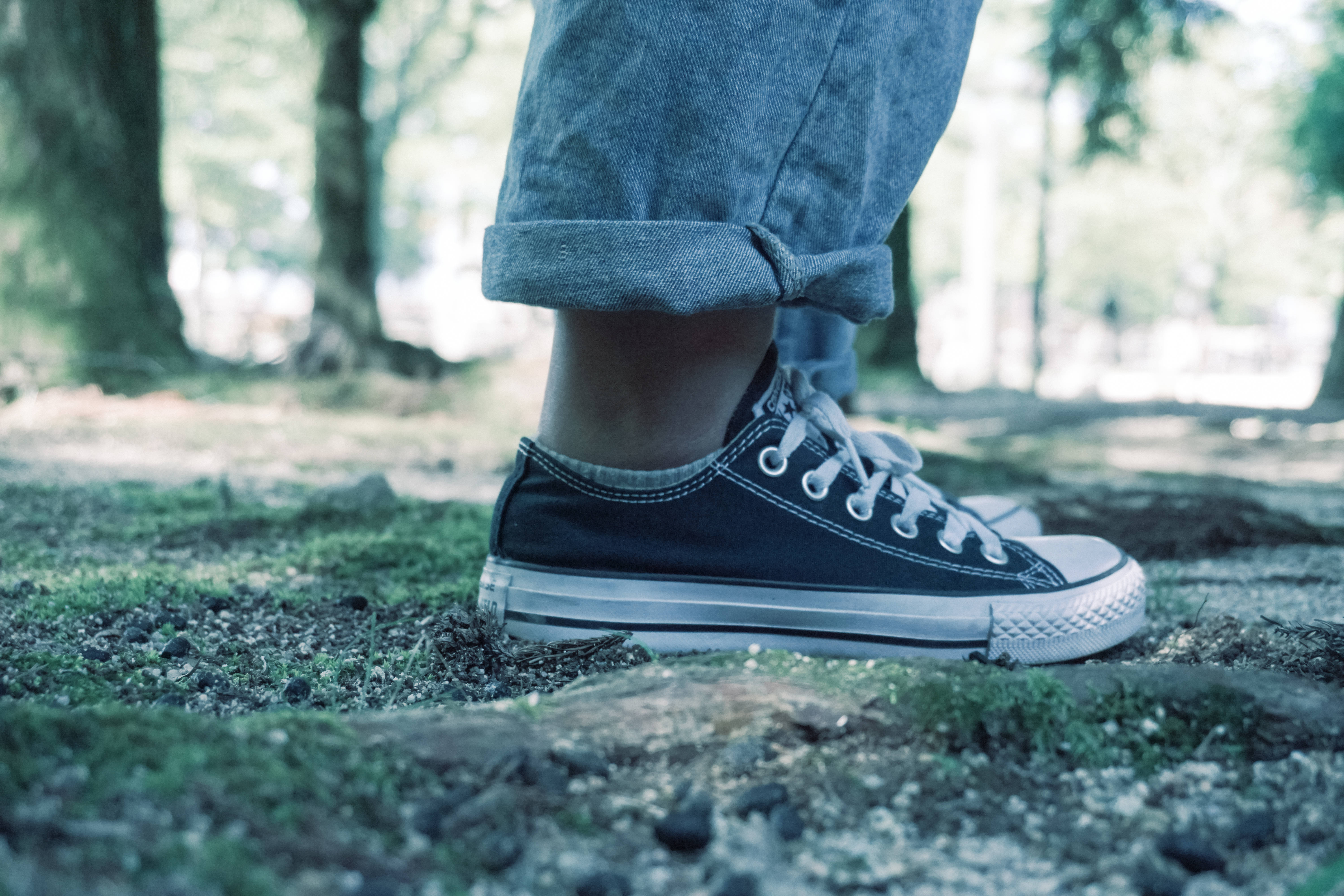Sneaker 桌布 壁紙 — 森林中，一個人穿著黑色運動鞋的腳部特寫，站在長滿苔蘚的地面上。