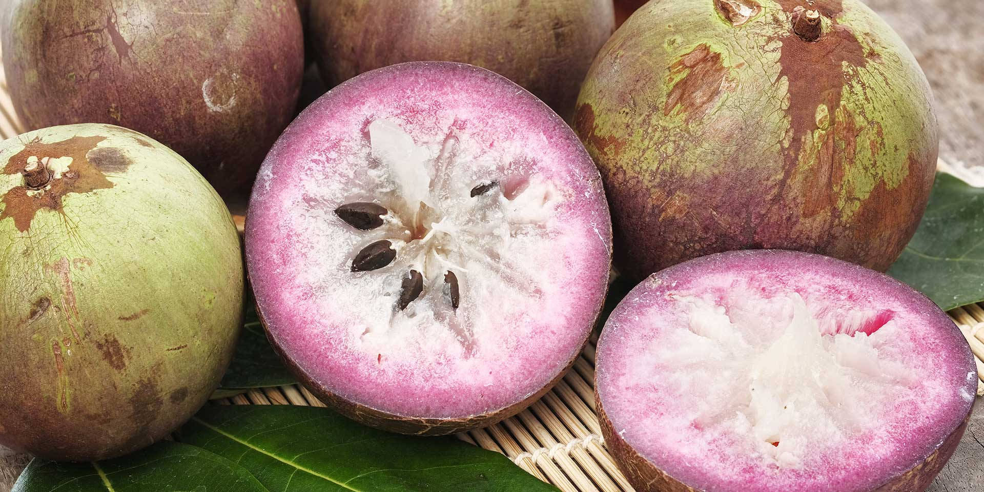 Fruit 桌布 壁紙 — 楊桃的特寫，帶有充滿活力的粉紅色果肉和深色種子，與完整的水果和綠葉一起放在編織墊上。