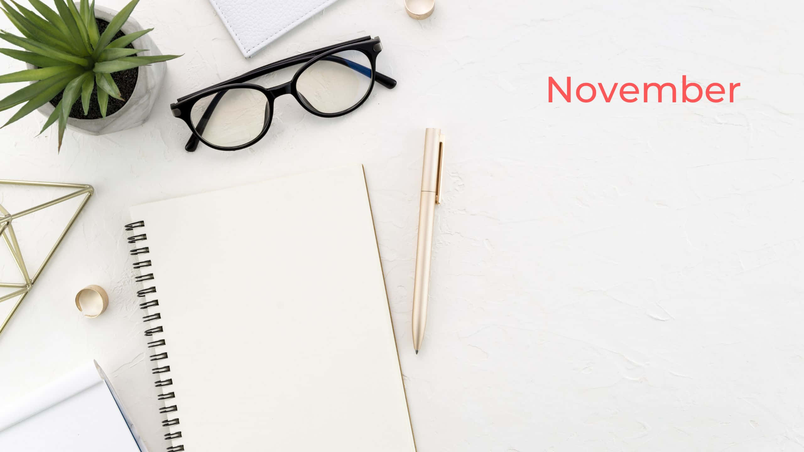 November Desktop 桌布 壁紙 — 極簡書桌設置，配有眼鏡、筆、筆記本和多肉植物，置於有紋理的白色表面上，帶有紅色十一月文字。