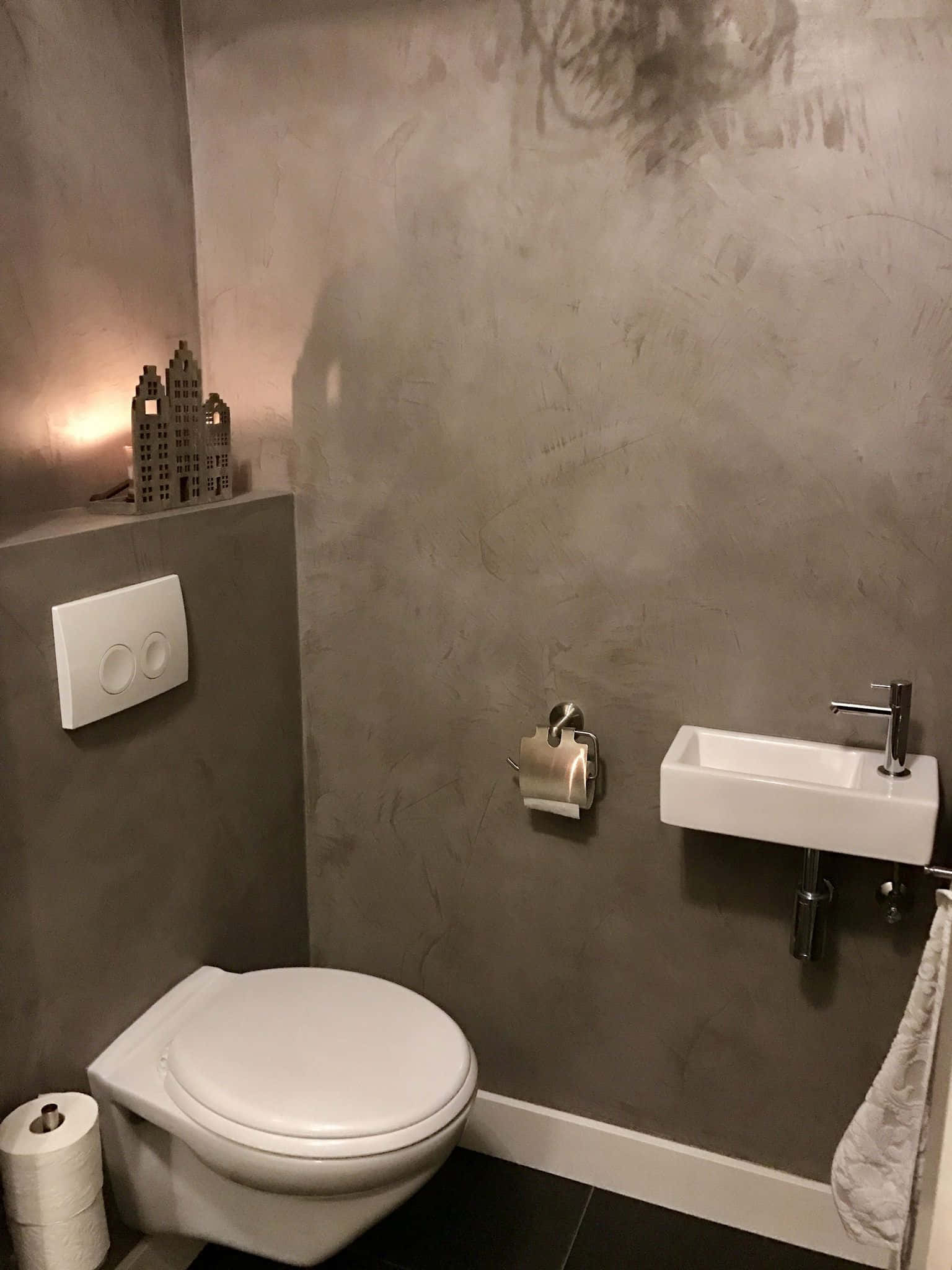 Toilet 桌布 壁紙 — 極簡浴室，配有紋理灰色牆壁、白色馬桶和洗手盆，以及來自城市景觀燈的溫暖環境照明。