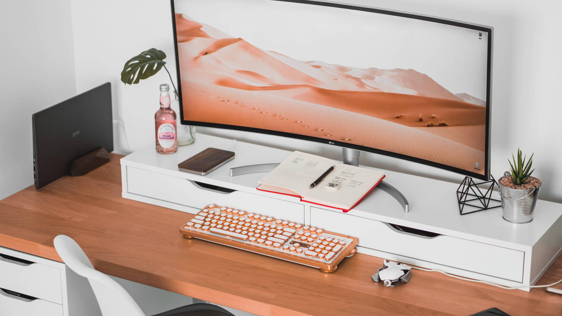 Office Desk 桌布 壁紙 — 極簡現代辦公桌設置，配備曲面顯示器顯示沙漠沙丘和珊瑚色鍵盤。
