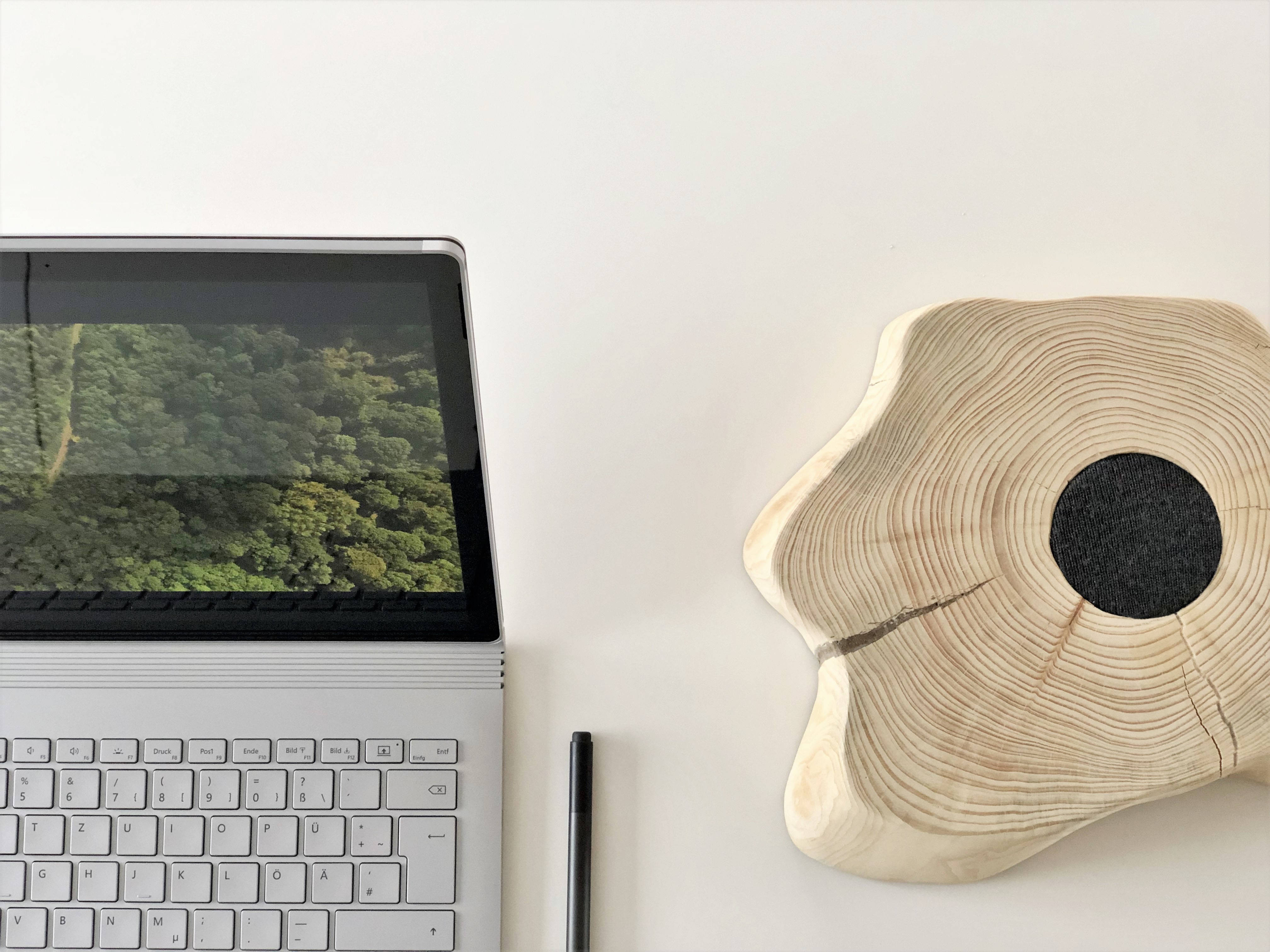 Surface 桌布 壁紙 — 極簡白色桌面設置，配備銀色筆記型電腦，顯示茂密綠色森林和獨特的黑色中心木片。