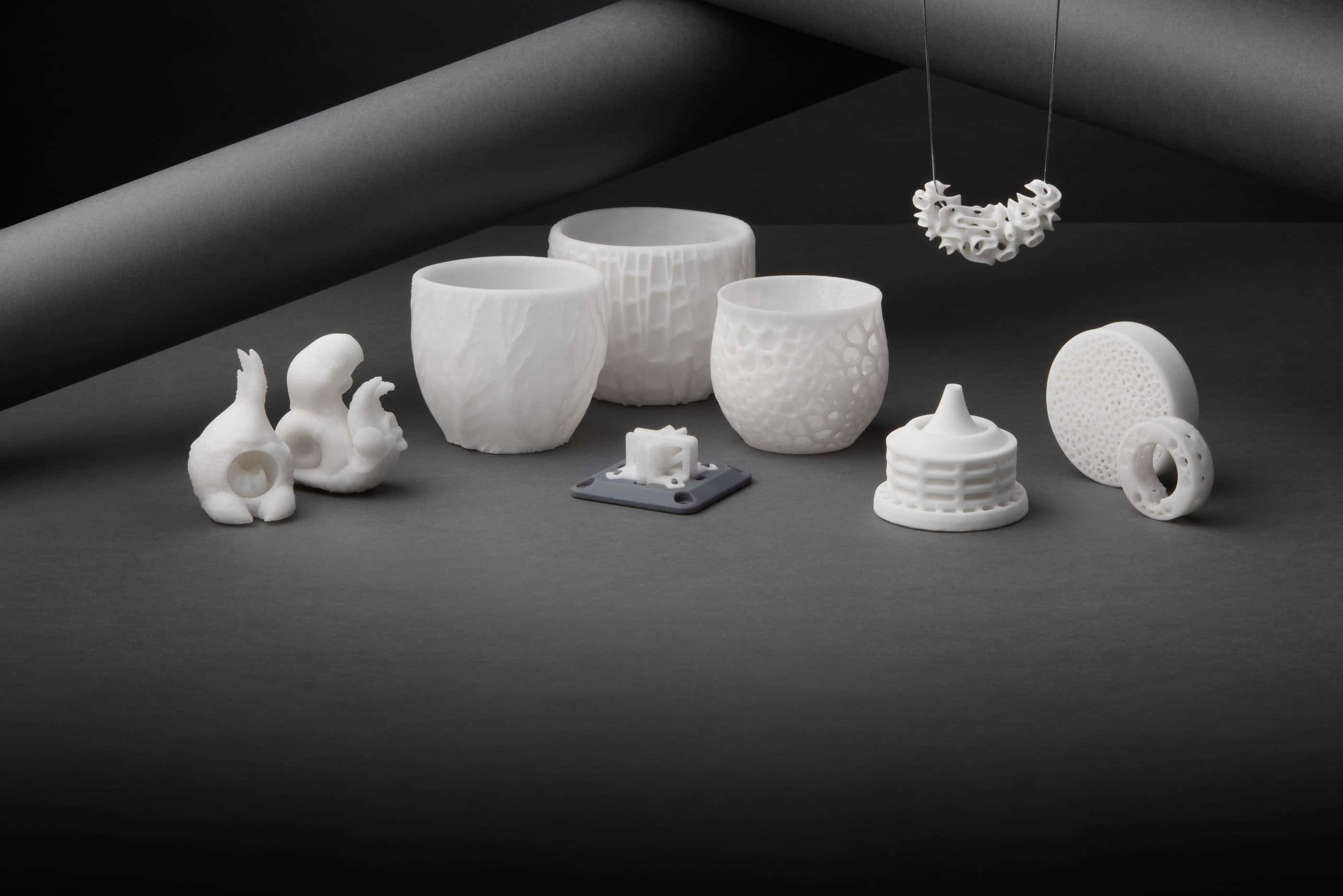 Ceramic 桌布 壁紙 — 極簡白色陶瓷雕塑和容器，帶有精緻紋理，在柔和的工作室燈光下排列在深灰色表面上。