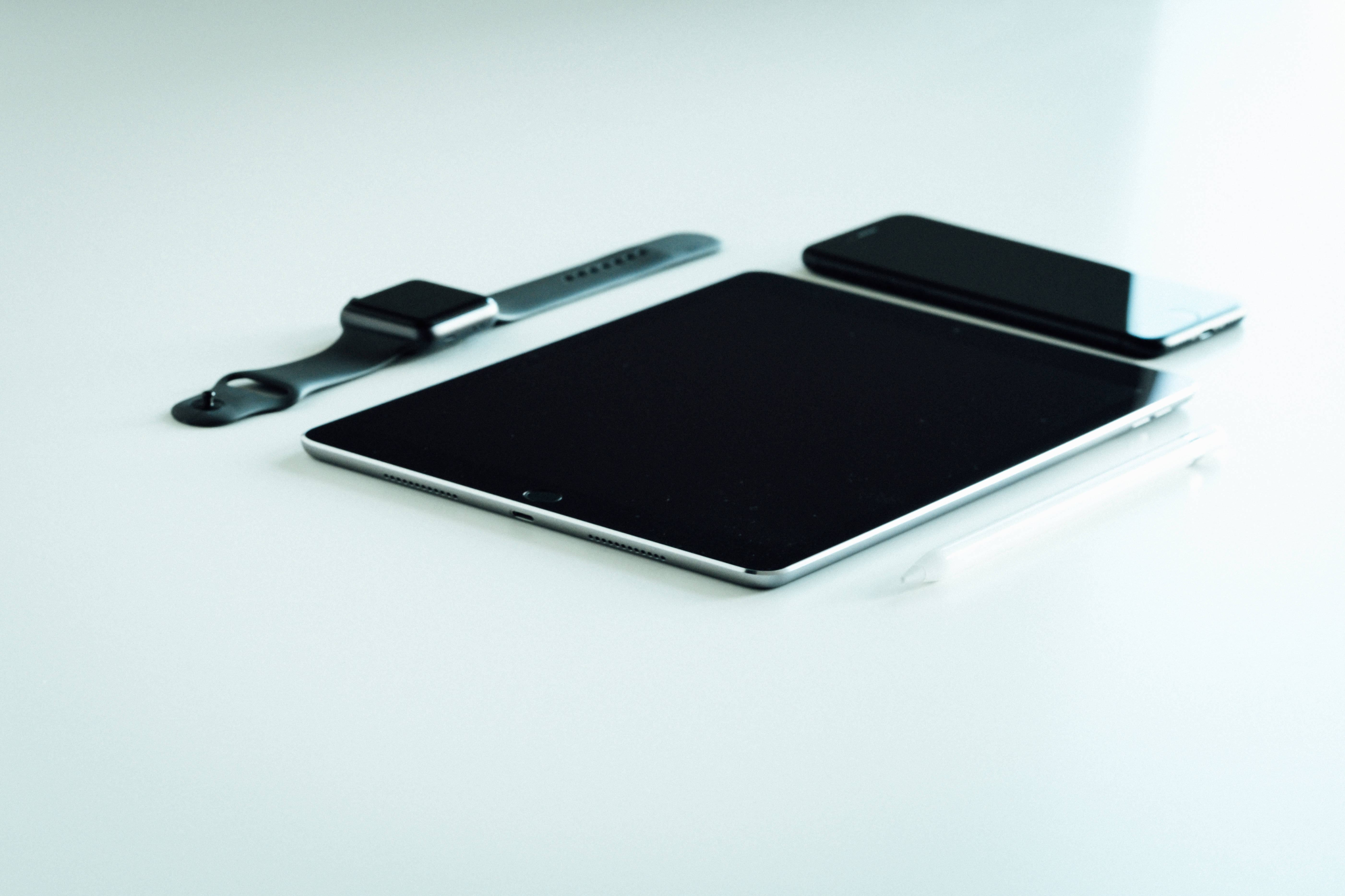 平板電腦 桌布 壁紙 — 極簡科技設置，平板電腦、智慧手錶和手機整齊排列在明亮的白色表面上。