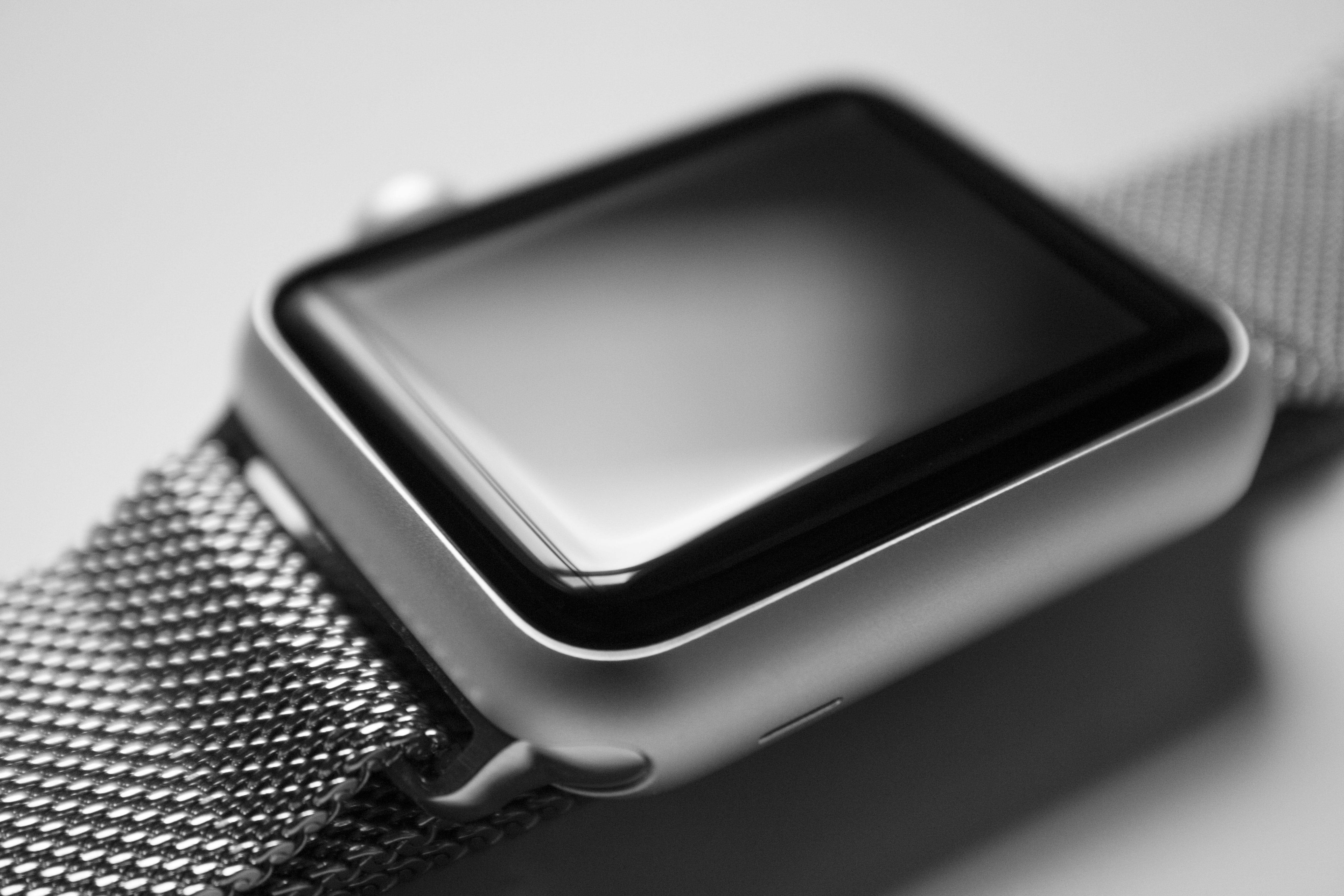 Apple Watch 動態 桌布 壁紙 — 極簡背景上，帶有網狀錶帶和反光螢幕的時尚銀色智慧手錶特寫。