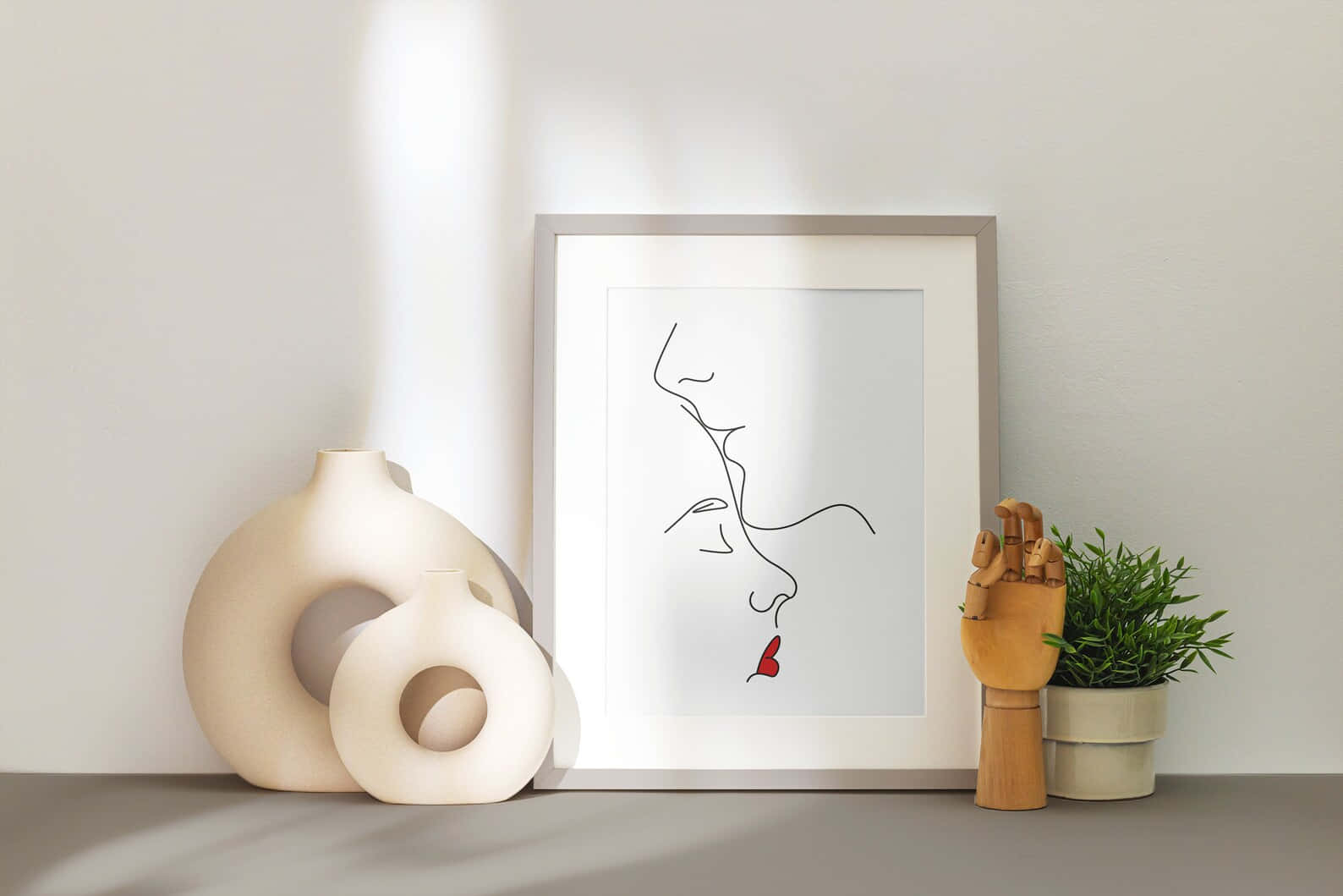 Forehead Kiss 桌布 壁紙 — 極簡風格框畫，描繪一張帶有紅唇的臉，放在架子上，旁邊有陶瓷花瓶和木手雕塑。