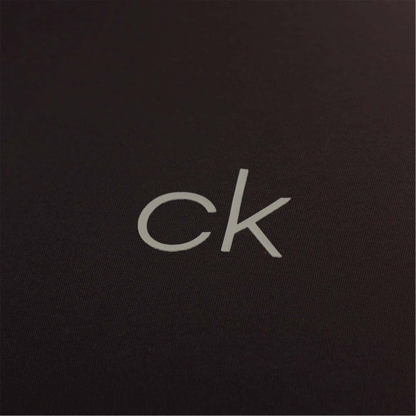 Calvin Klein 桌布 壁紙 — 極簡風格特寫，銀色 'ck' 標誌位於有紋理的黑色布料上，光線柔和。